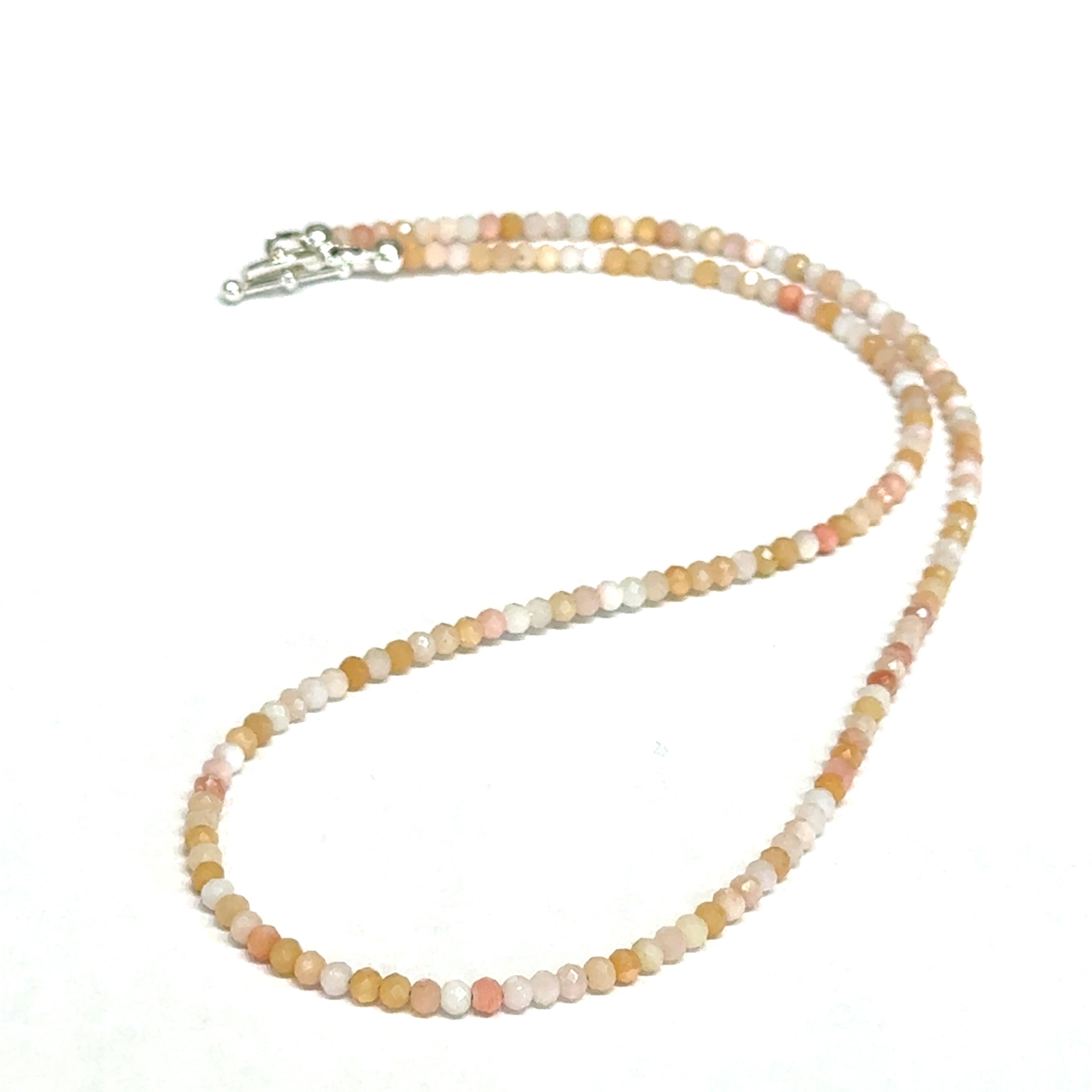 Close-up of faceted pink opal gemstone beads catching light on delicate beaded necklace on a white background, front view.
