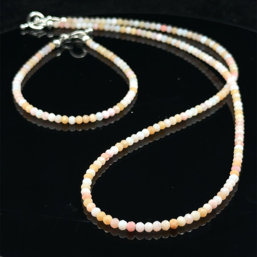 Close-up of faceted pink opal gemstone beads catching light on delicate beaded necklace with it's matching bracelet on a black background, front view. 