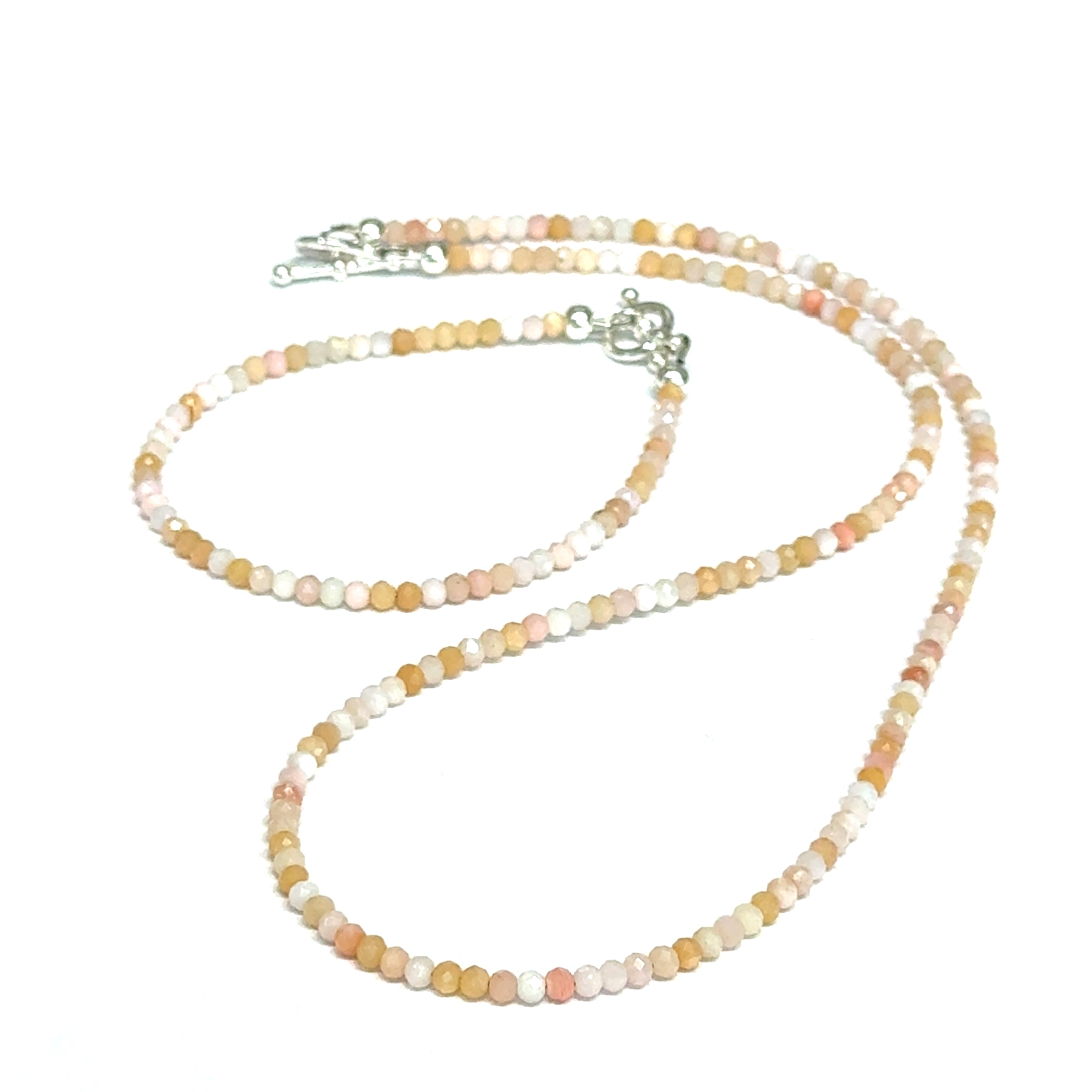 Close-up of faceted pink opal gemstone beads catching light on delicate beaded necklace with it's matching bracelet on a white background, front view.