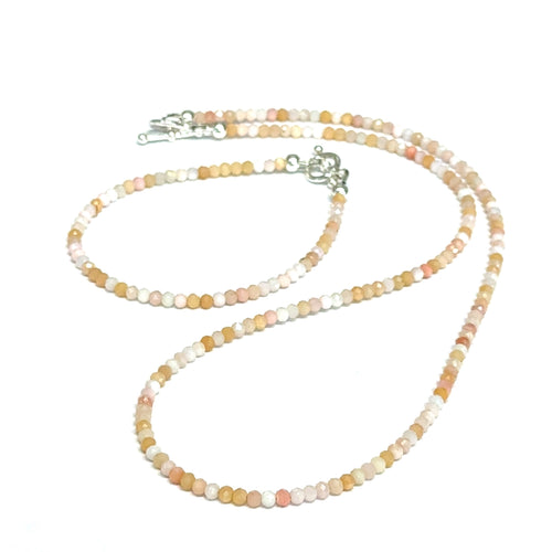 Close-up of faceted pink opal gemstone beads catching light on delicate beaded necklace with it's matching bracelet on a white background, front view.
