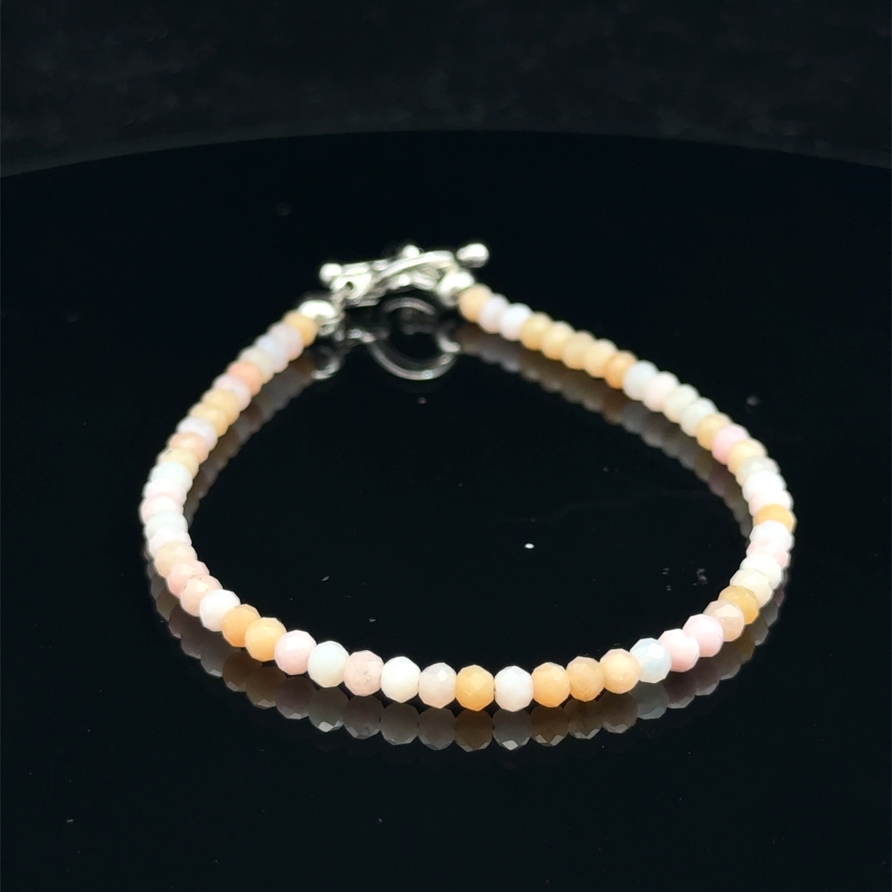 Close-up of faceted pink opal gemstone beads on a delicate beaded bracelet with a handcrafted toggle on a black  background, front view. 