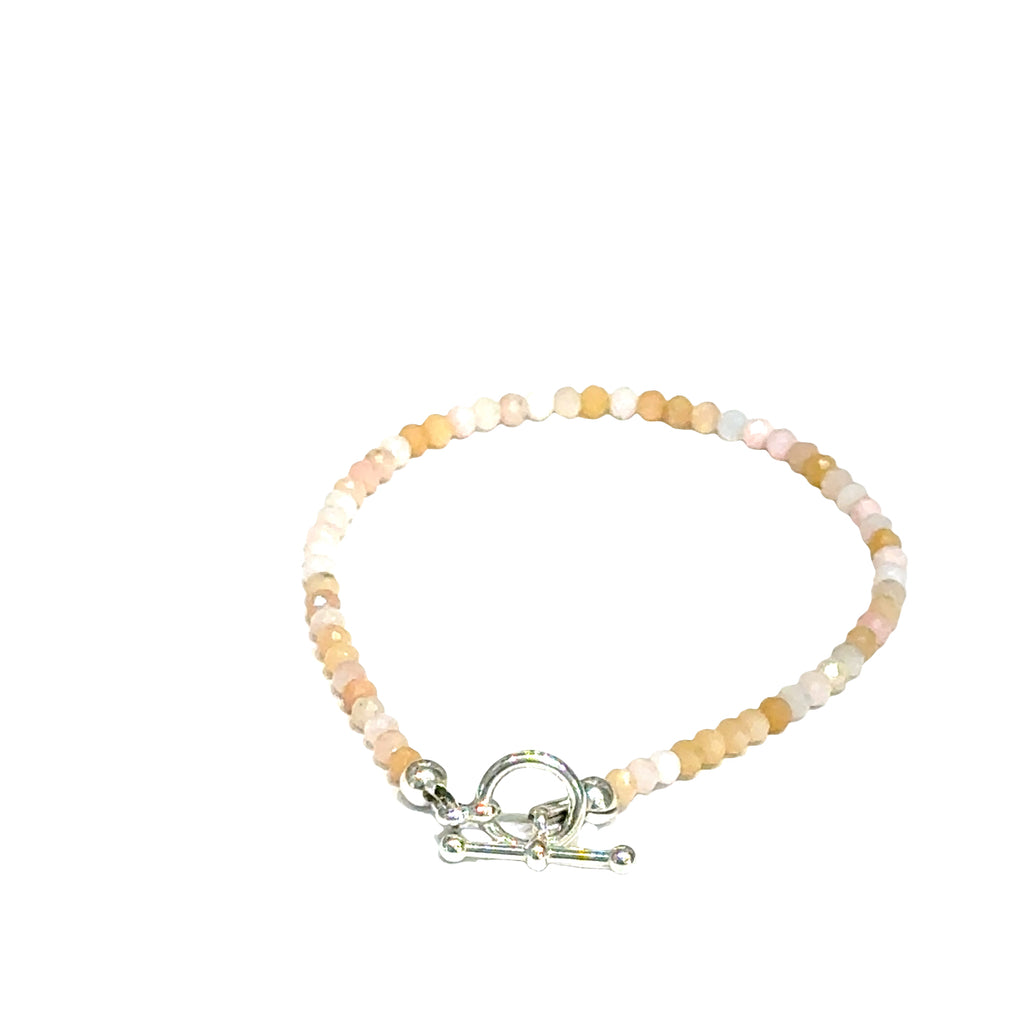 Close-up of faceted pink opal gemstone beads on delicate beaded bracelet with handcrafted toggle on a white background, back toggle view. 