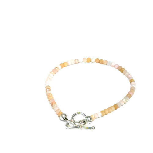 Close-up of faceted pink opal gemstone beads on delicate beaded bracelet with handcrafted toggle on a white background, back toggle view. 