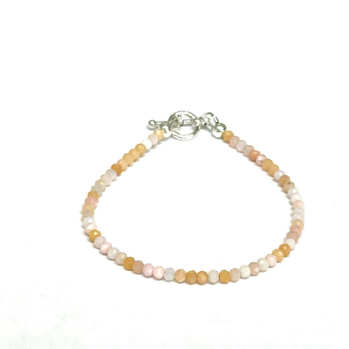 Close-up of faceted pink opal gemstone beads on a delicate beaded bracelet with a handcrafted toggle on a white background, front view. 