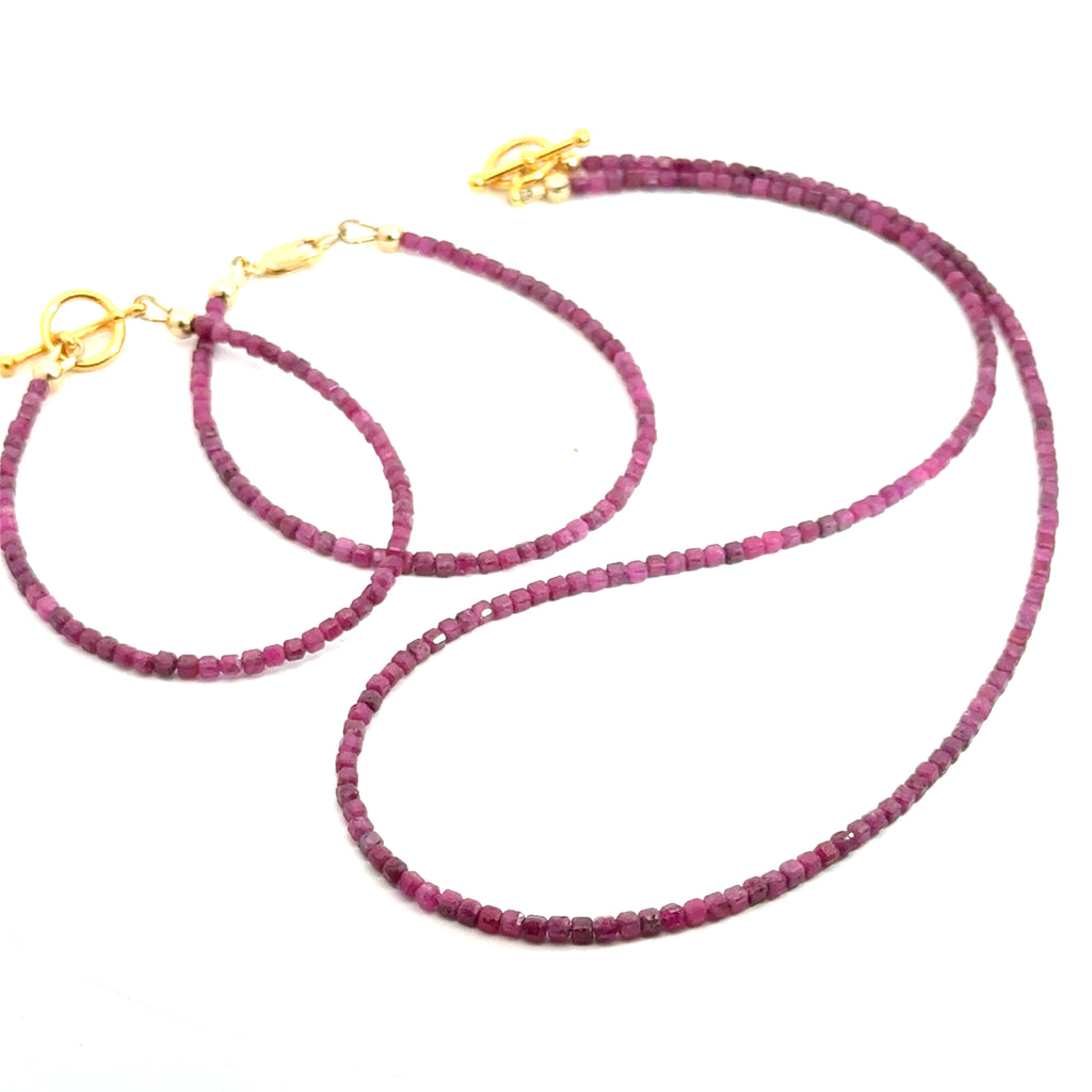 Close-up of faceted ruby cubed beaded bracelets with a matching necklace showing deep red hues and natural shine on a white background, front overview.