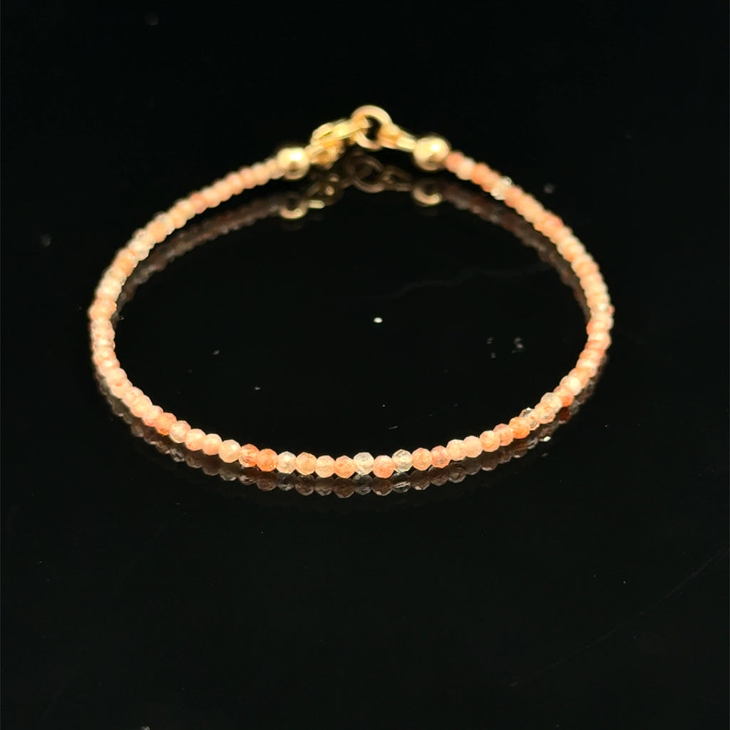 Close-up of faceted sunstone gemstone beads on delicate beaded bracelet with natural shimmer and gold-filled clasp on a black background, front view. 