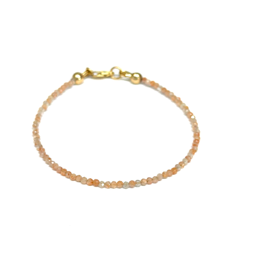 Close-up of faceted sunstone gemstone beads on delicate beaded bracelet with natural shimmer and gold-filled clasp on a white background, front view. 