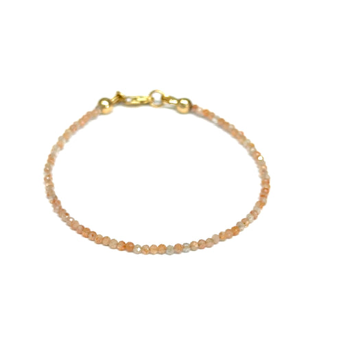 Close-up of faceted sunstone gemstone beads on delicate beaded bracelet with natural shimmer and gold-filled clasp on a white background, front view. 