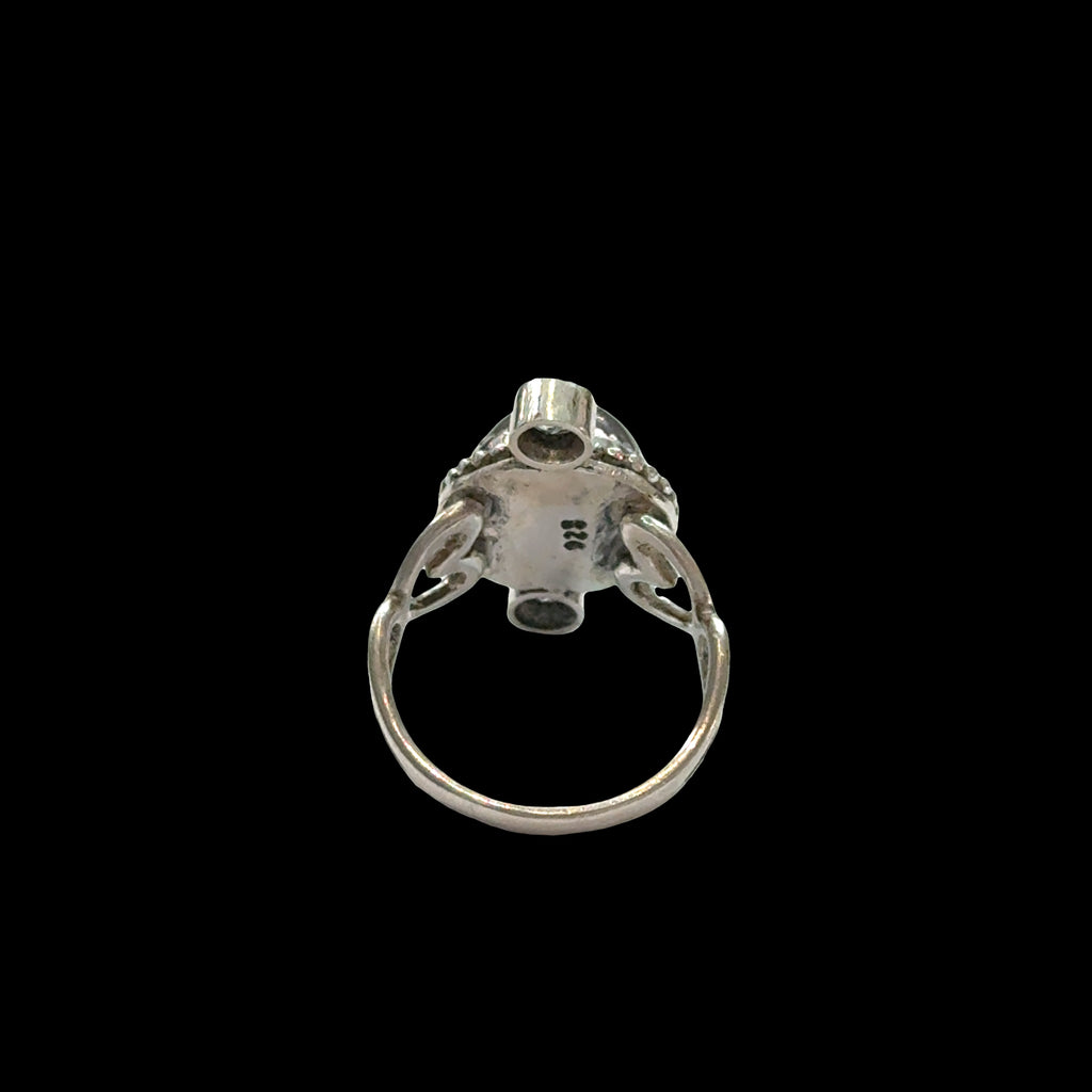 Close-up of grey moonstone adularescence glow with faceted blue topaz accents, sterling silver decorative bezel, spiritual ring on a black background, back side view.