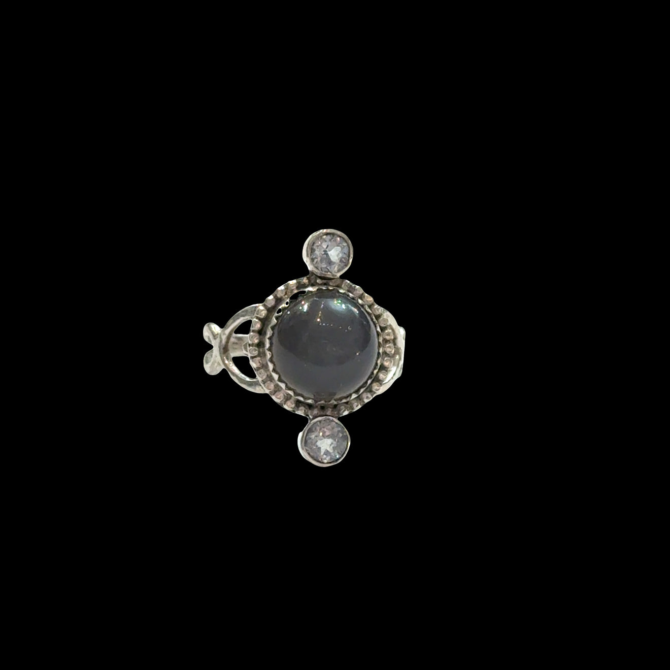 Close-up of grey moonstone adularescence glow with faceted blue topaz accents, sterling silver decorative bezel, spiritual ring on a black background, front view. 