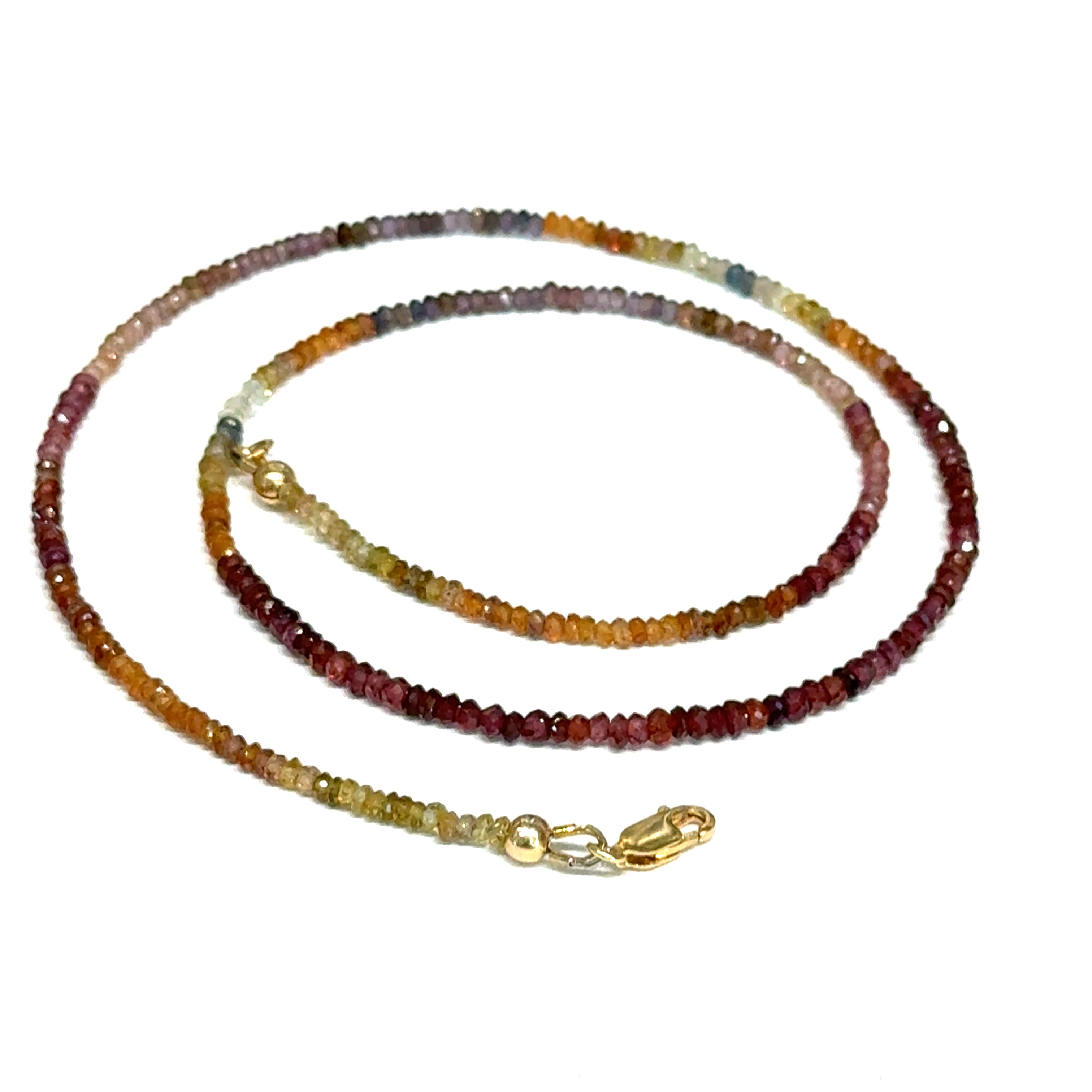 Close-up of natural brown sapphire beads showing honey amber to chocolate color variations, on a white background,  in a spiral claps view. 