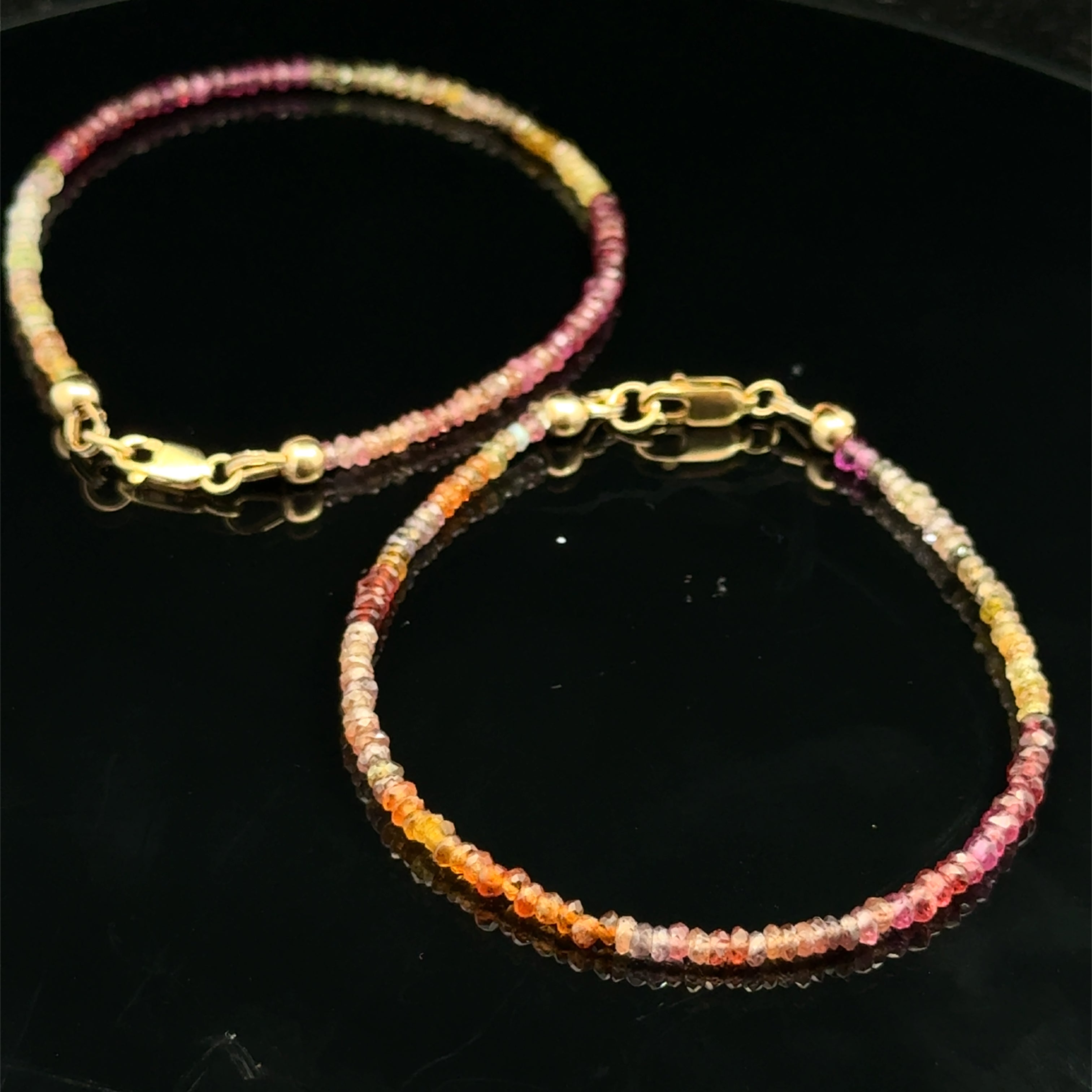 Close-up of two natural brown sapphire beads showing honey amber to chocolate color variations, on a black background, overview.
