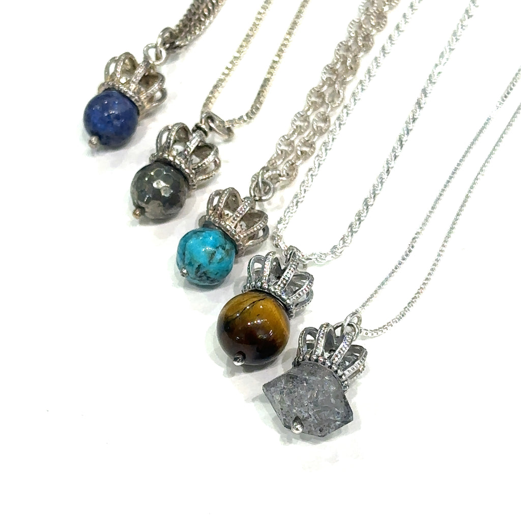Collection of gemstone crown pendants (Pyrite, Turquoise, Tiger Eye, Herkimer Diamond) on a white background, hanging, front overview. 