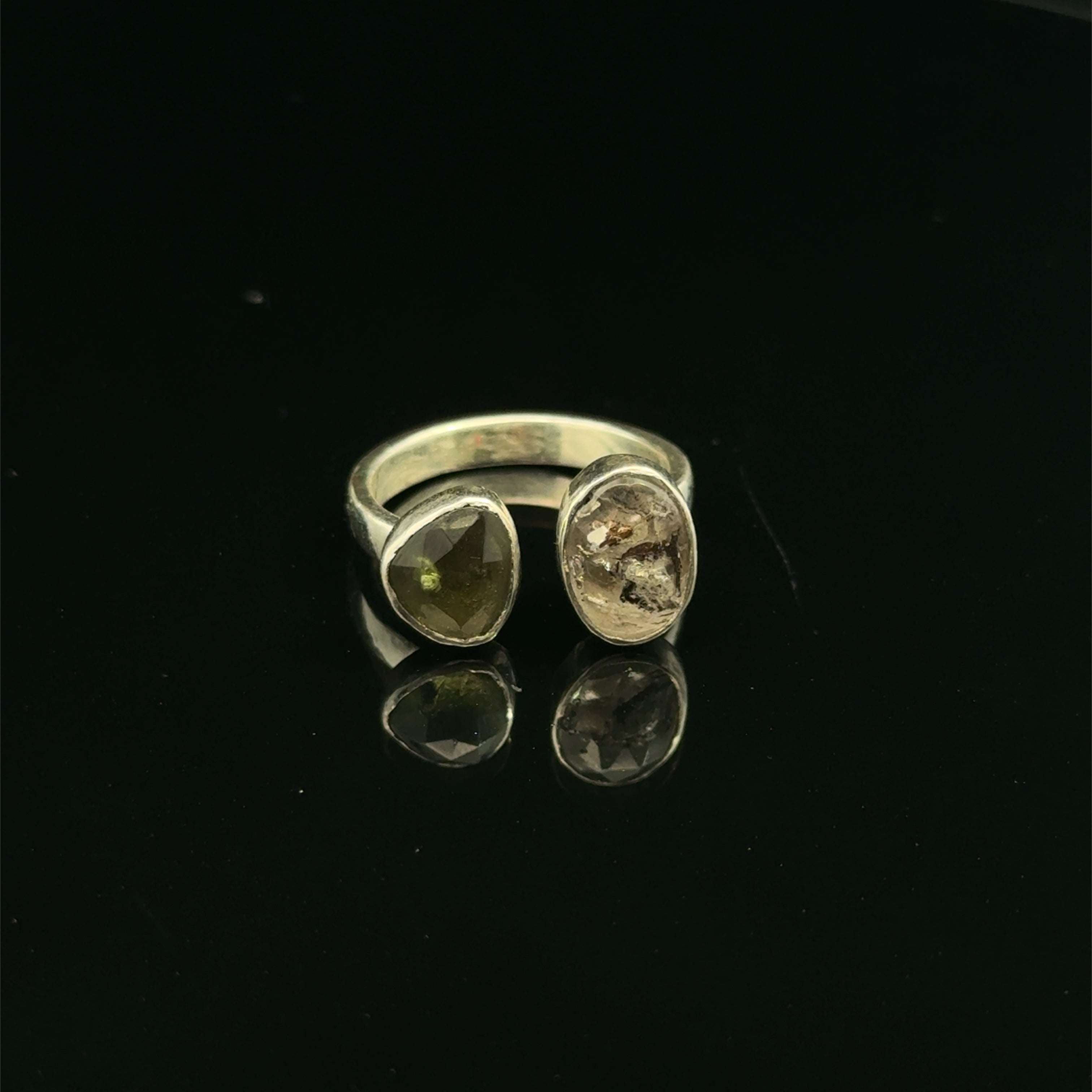 Detailed view of faceted Moldavite and Herkimer Diamond gemstones bezel-set in sterling silver, showing radiant green and clear crystal brilliance on a black background front center view. 