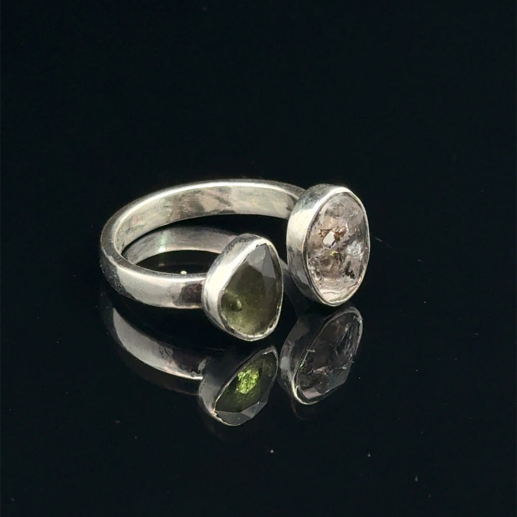 Detailed view of faceted Moldavite and Herkimer Diamond gemstones bezel-set in sterling silver, showing radiant green and clear crystal brilliance on a black background left side front view. 