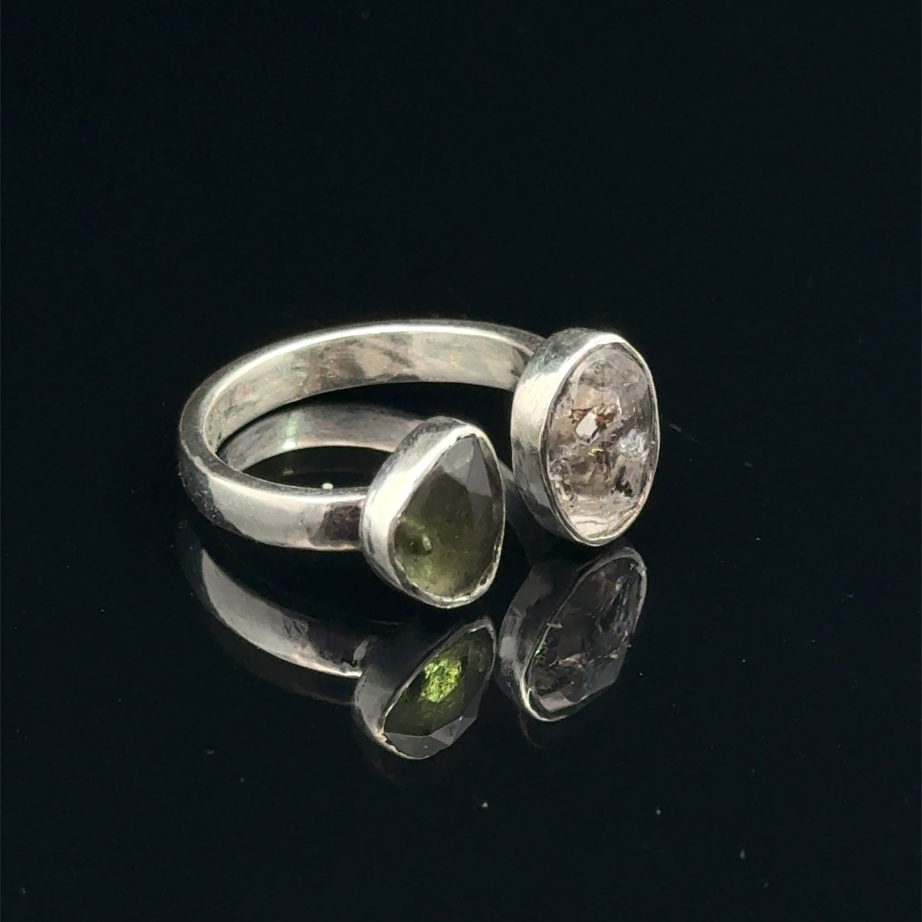 Detailed view of faceted Moldavite and Herkimer Diamond gemstones bezel-set in sterling silver, showing radiant green and clear crystal brilliance on a black background left side front view. 