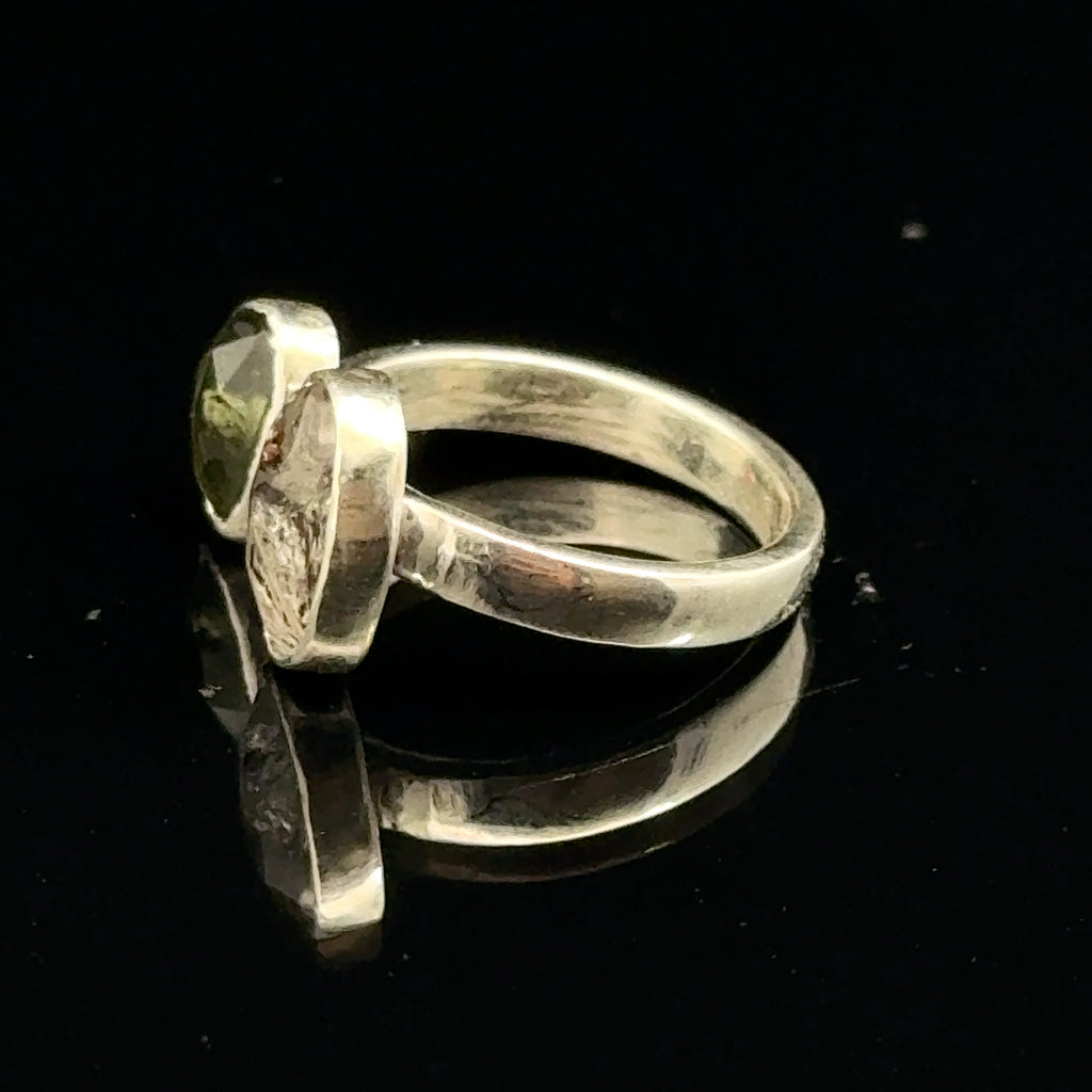 Detailed view of faceted Moldavite and Herkimer Diamond gemstones bezel-set in sterling silver, showing radiant green and clear crystal brilliance on a black background left side view. 