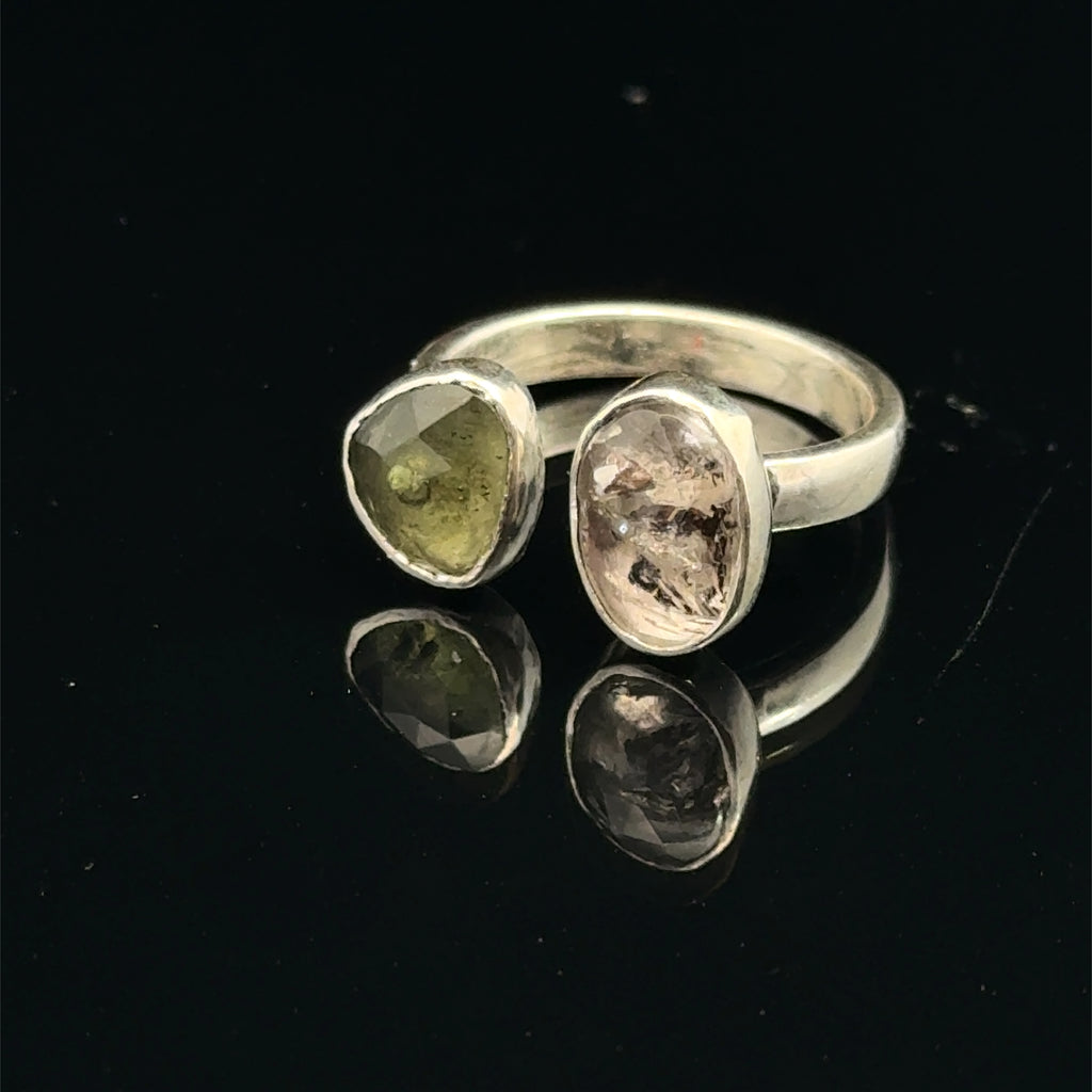 Detailed view of faceted Moldavite and Herkimer Diamond gemstones bezel-set in sterling silver, showing radiant green and clear crystal brilliance on a black background slight left angle front view. 
