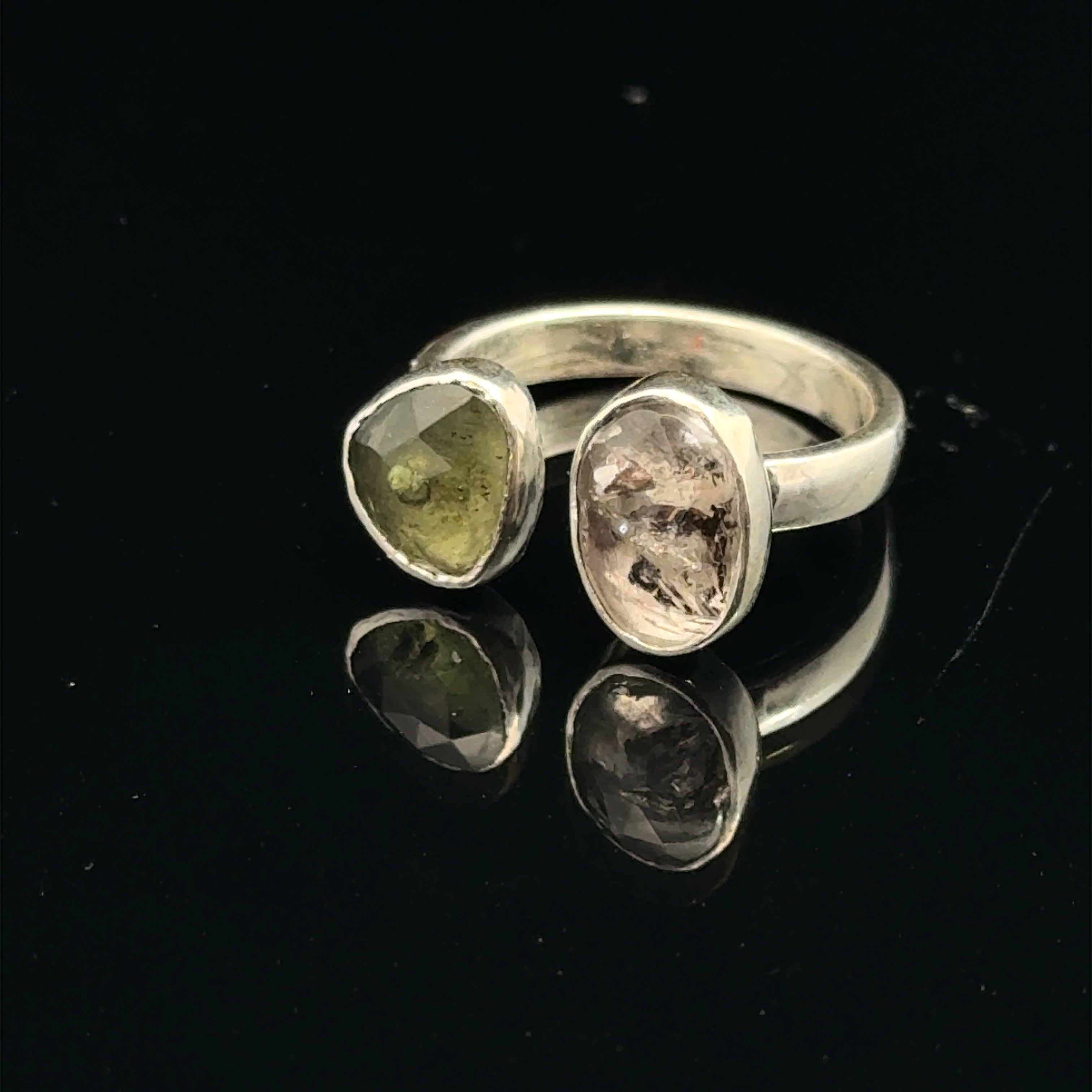 Detailed view of faceted Moldavite and Herkimer Diamond gemstones bezel-set in sterling silver, showing radiant green and clear crystal brilliance on a black background slight left angle front view. 