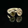 Detailed view of faceted Moldavite and Herkimer Diamond gemstones bezel-set in sterling silver, showing radiant green and clear crystal brilliance on a black background slight right angle front view. 