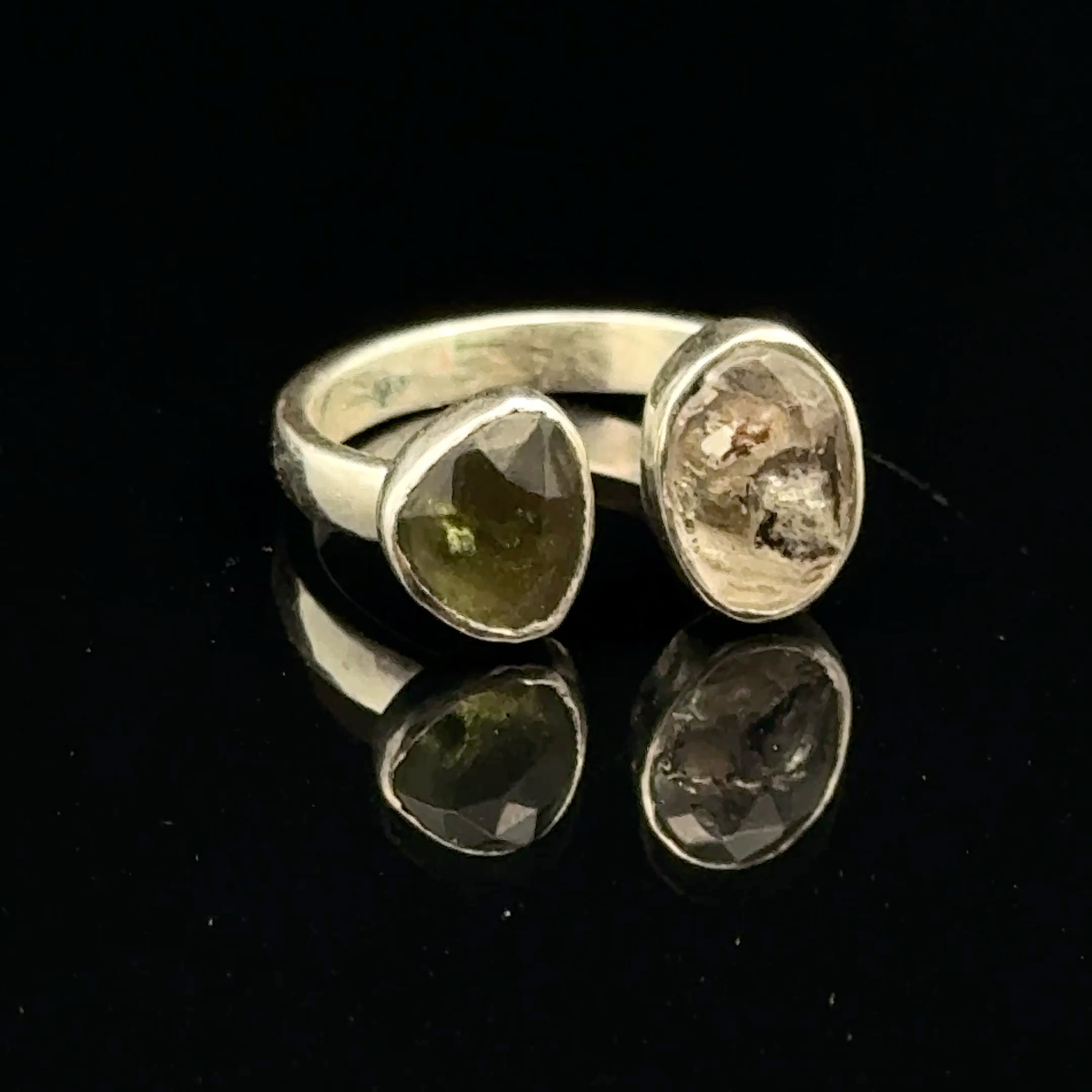 Detailed view of faceted Moldavite and Herkimer Diamond gemstones bezel-set in sterling silver, showing radiant green and clear crystal brilliance on a black background slight right angle front view. 