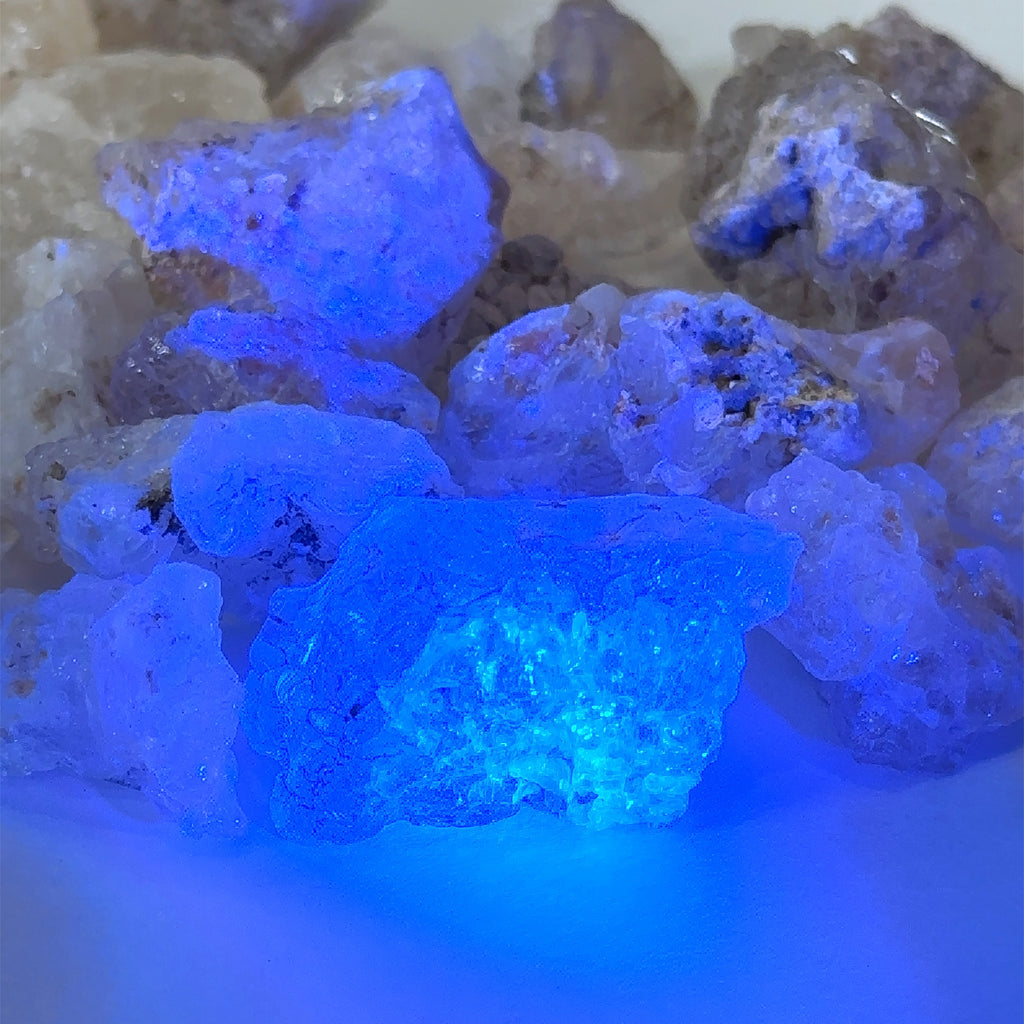 Ethically sourced raw Hyalite Opal gemstone with luminous glow grouping of  on white with a blue light overview