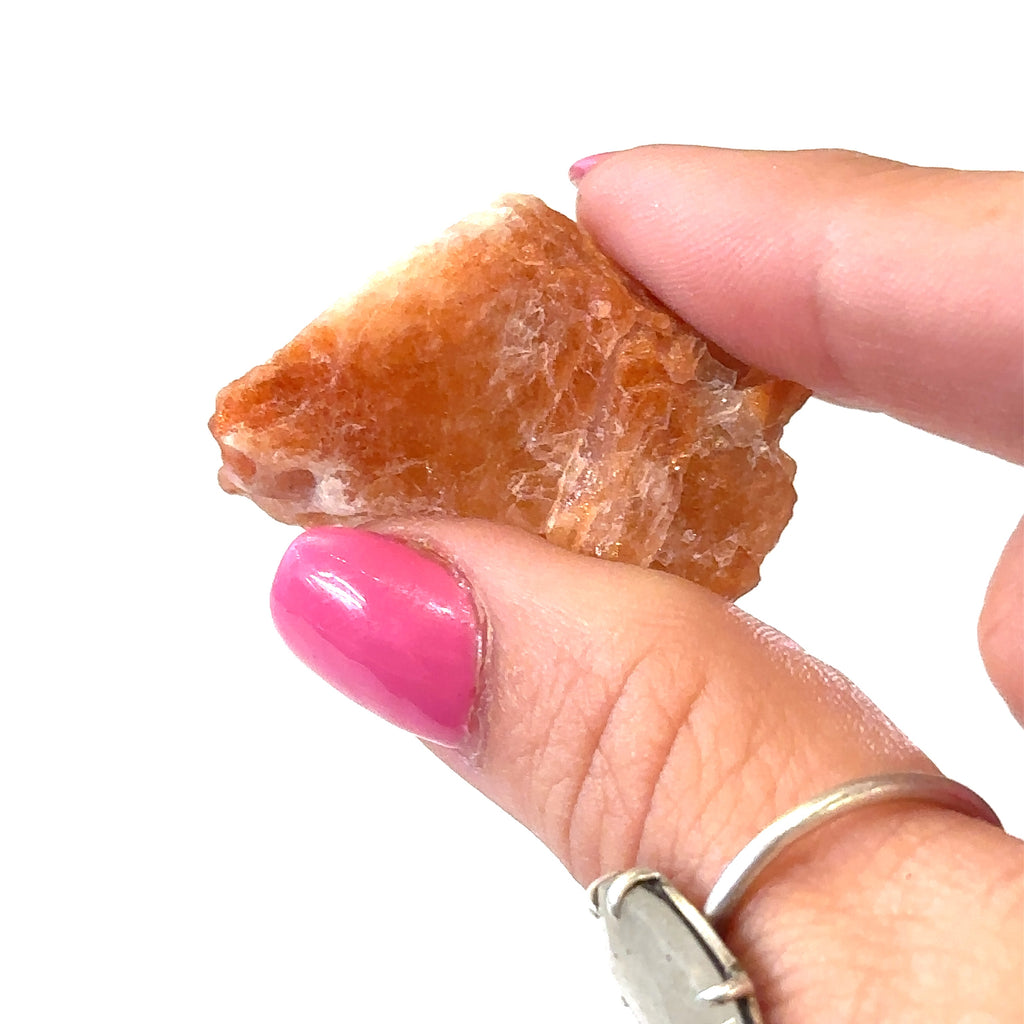 Ethically sourced raw sunstone gemstone with natural orange hues on white in hand for close up view 