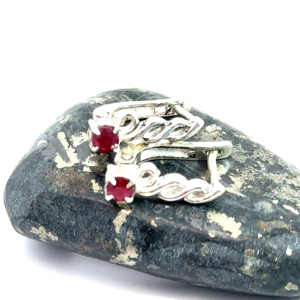 Faceted Ruby Snap‑Back Earrings on white and on rock sideway front view