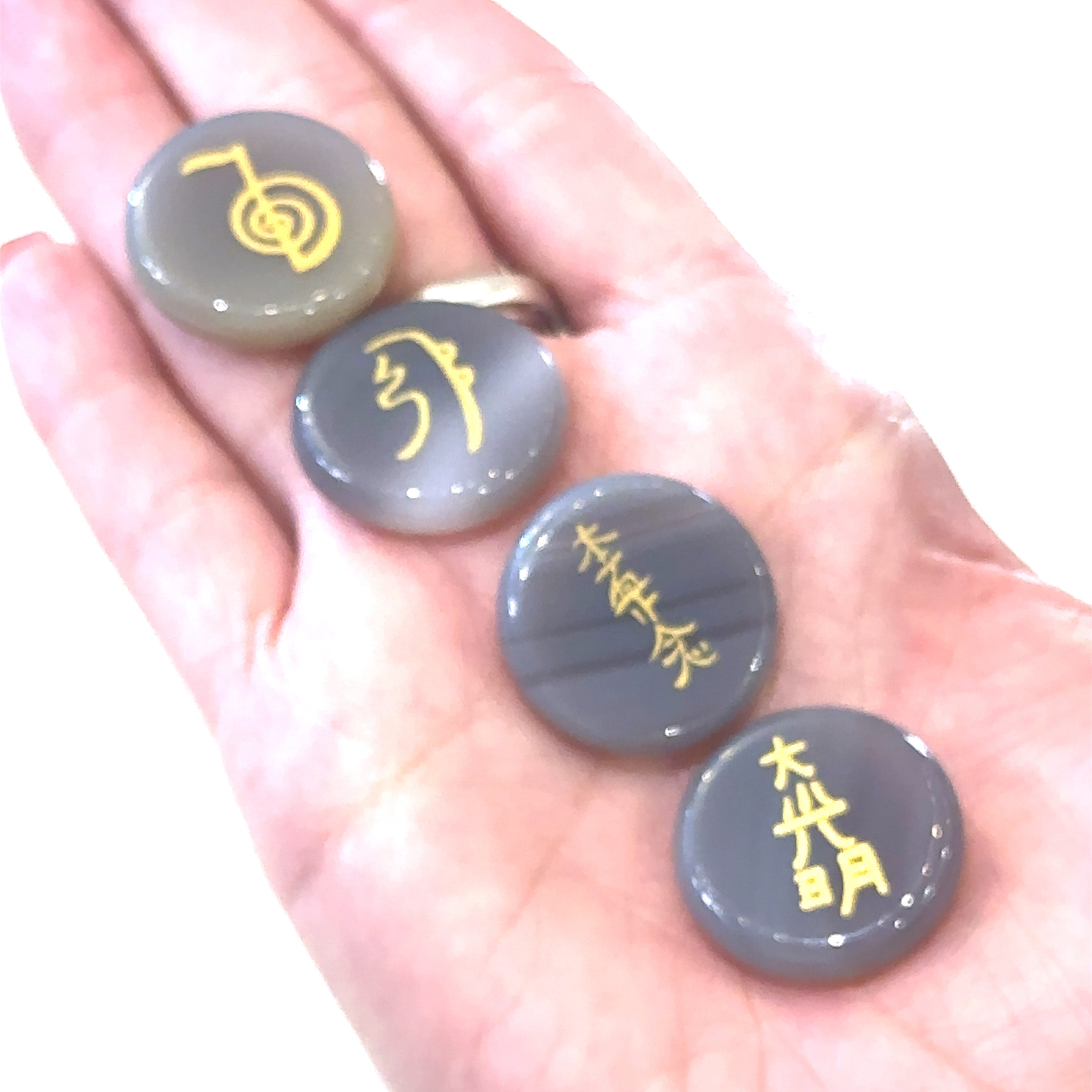 Four Botswana Agate gemstones with gold foil etching, each inscribed with a different Reiki symbol, are held in a model's hand—front view.