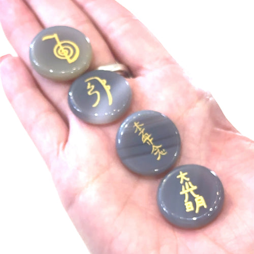 Four Botswana Agate gemstones with gold foil etching, each inscribed with a different Reiki symbol, are held in a model's hand—front view.