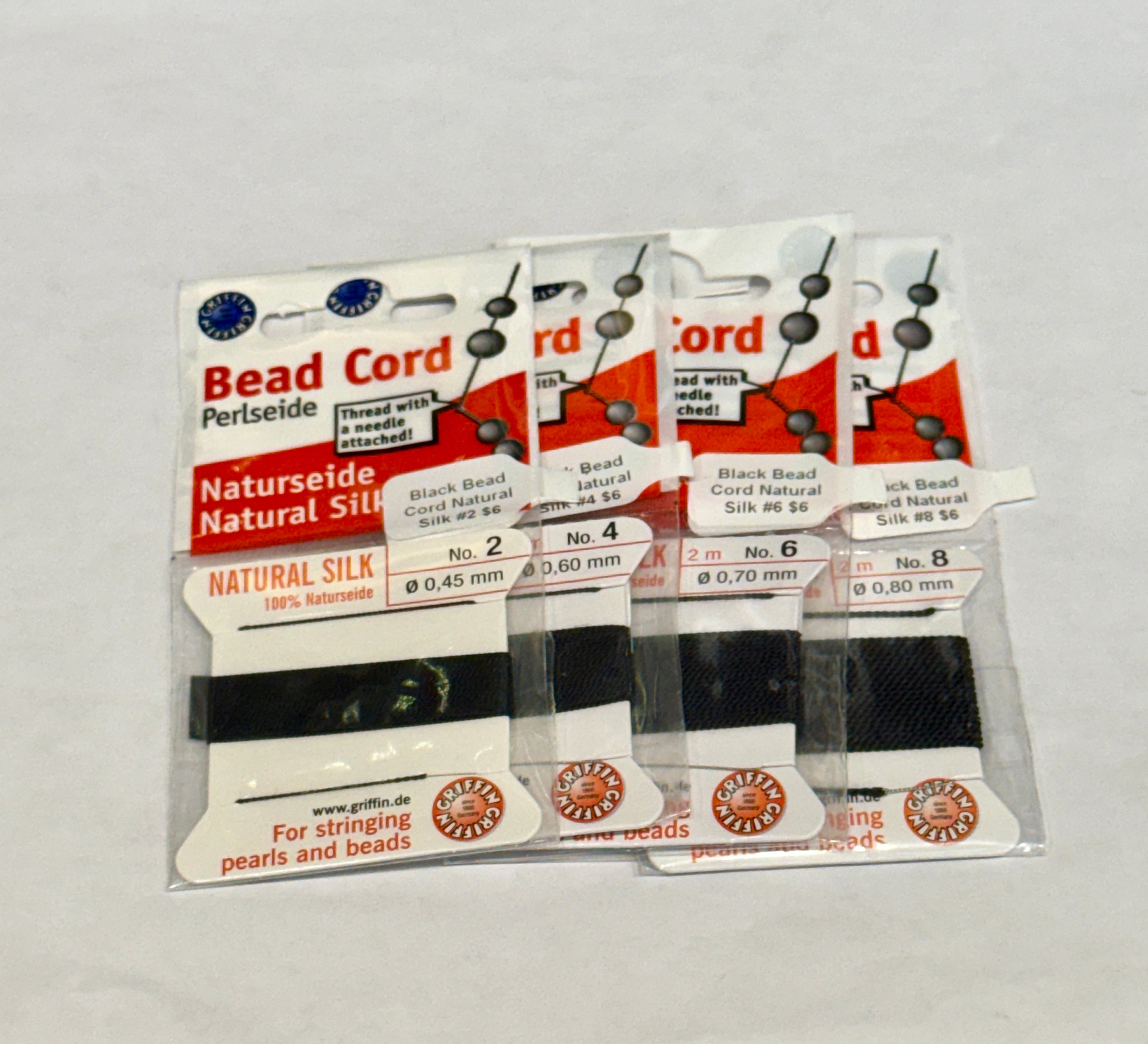 Four packages of Black Natural Silk Bead Cord  #2, 4,  6, & 8 on a white background, front view.