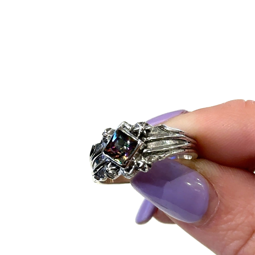 Hand-forged Mystic Topaz ring with shimmering colors under natural light in fingertips for a view of a close up view
