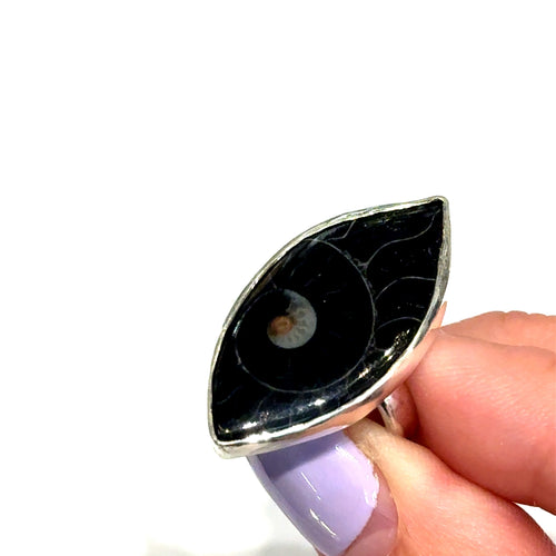 Hand holding a black and silver ring with a unique design on a white background, front top view. 
