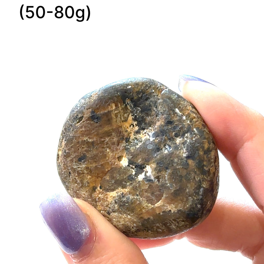 Hand holding raw Golden Sapphire stone to show natural size and texture of (50-80g) on white overview