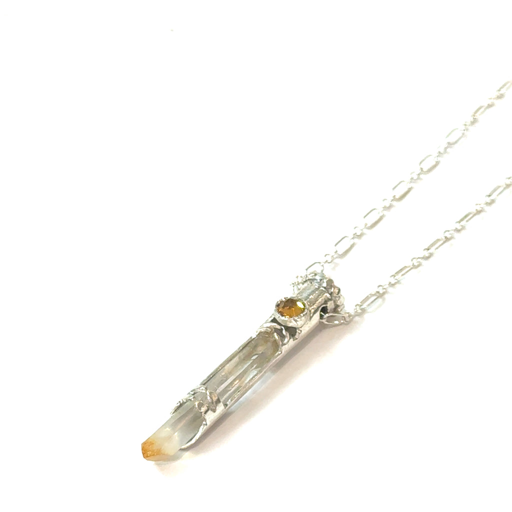 Mango Quartz Lightsaber Necklace in a Sterling Silver case with citrine gemstones to accent the pendant on a white background, in a models finger tips, front right angle hanging view. 