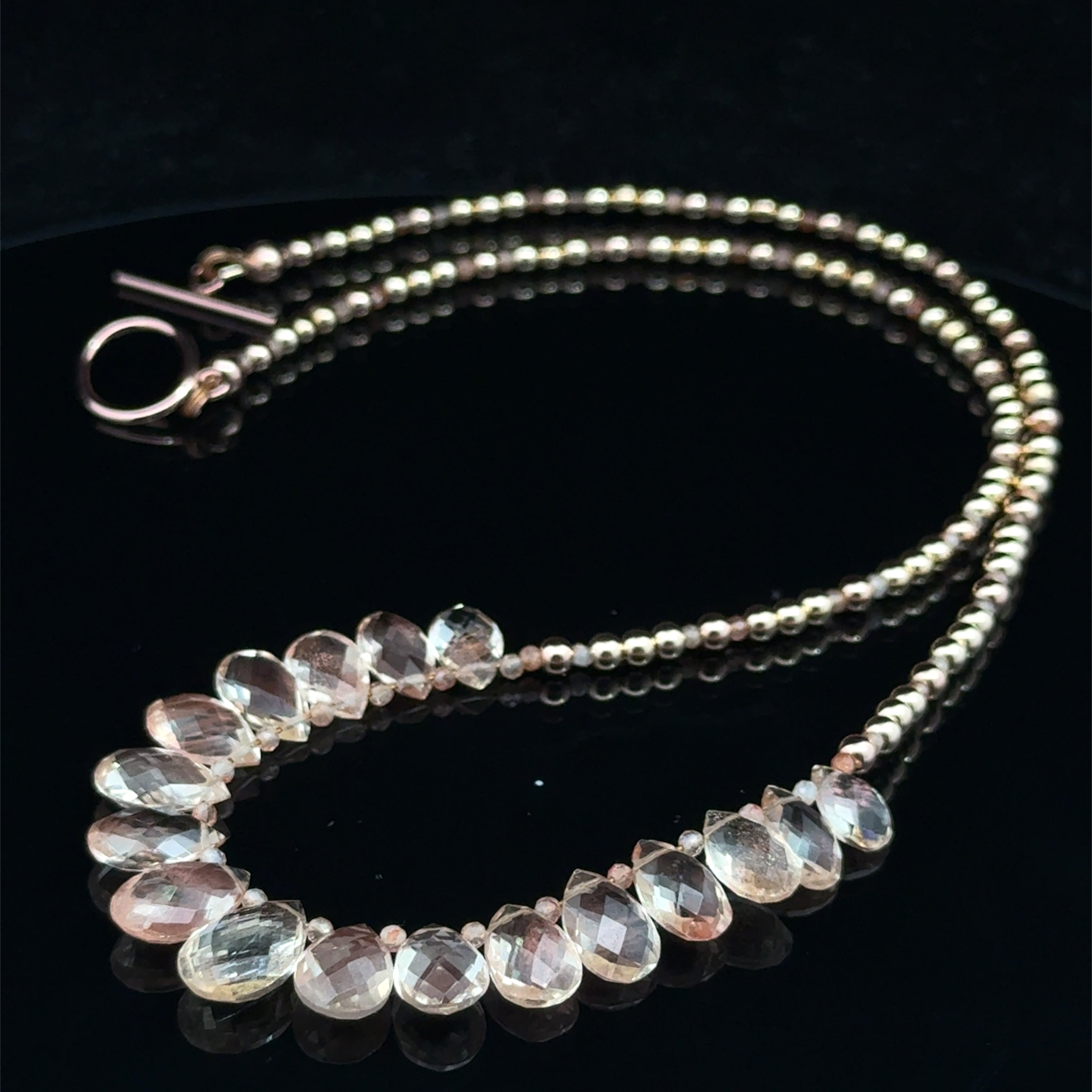 Oregon sunstone teardrop statement necklace with faceted focal stone and mixed metal sunstone beads showing peachy-copper brilliance on a black background, front close up view. 