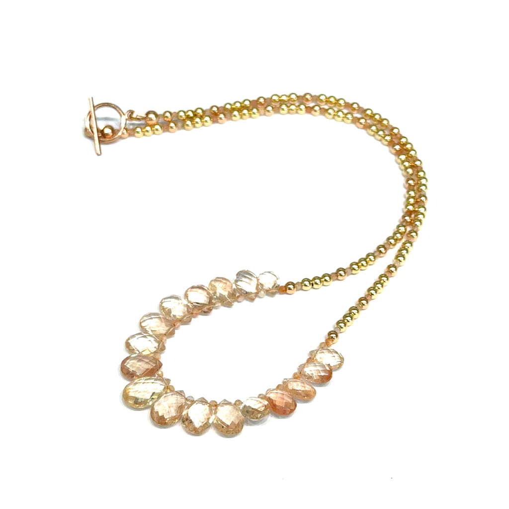 Oregon sunstone teardrop statement necklace with faceted focal stone and mixed metal sunstone beads showing peachy-copper brilliance on a white background, front close up view. 