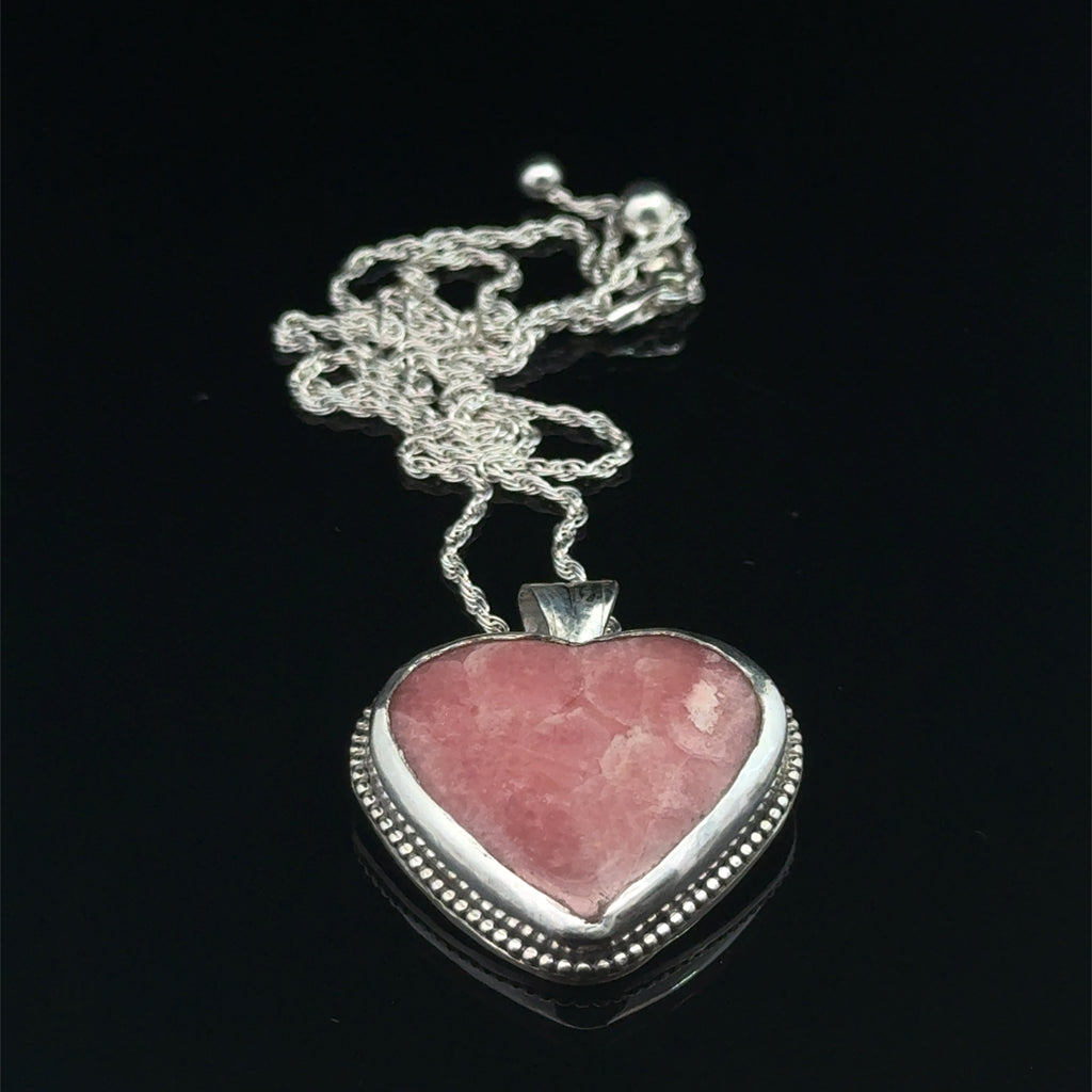 Pink Cobolto Calcite Heart-shaped gemstone pendant on a silver chain against a black background, front overview. 