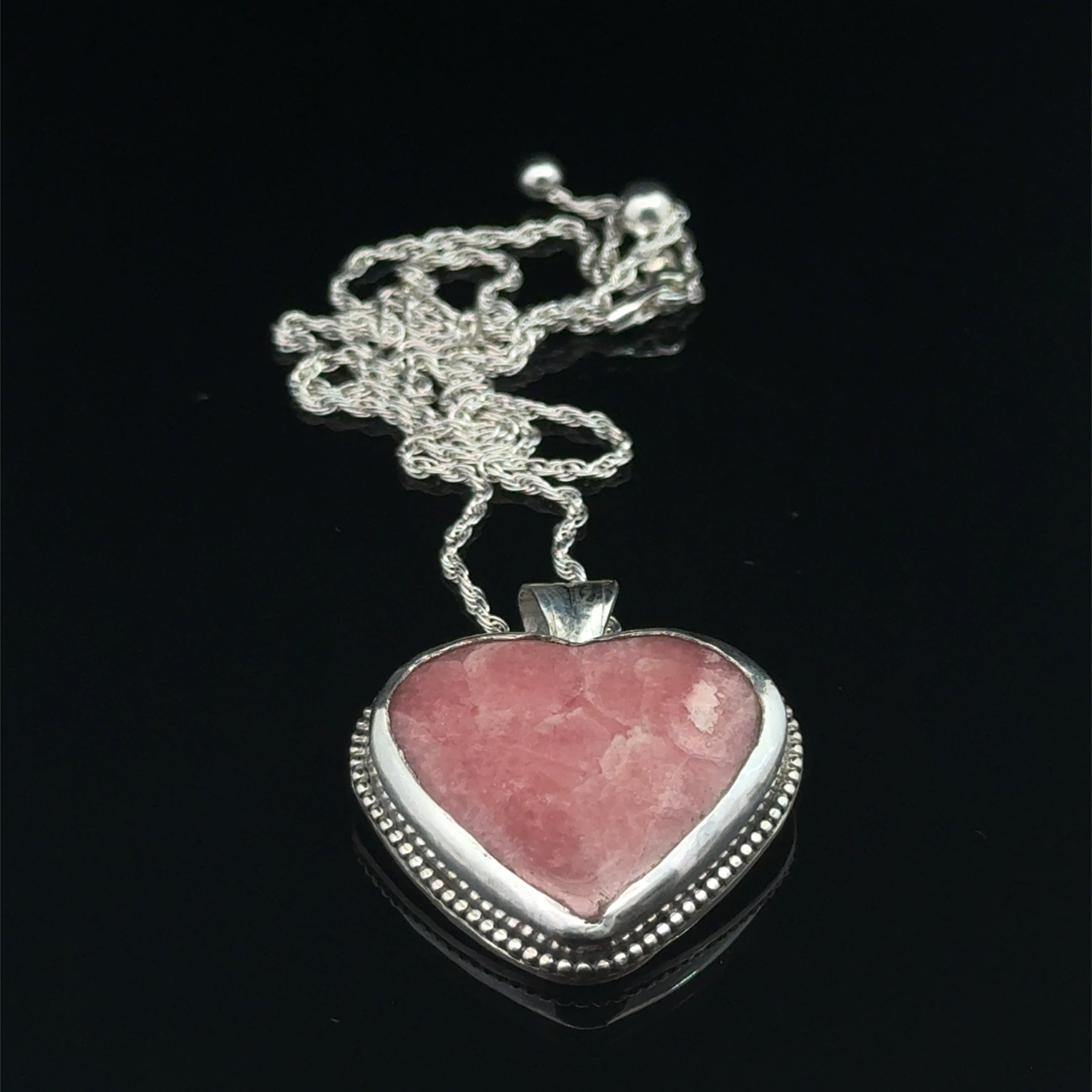 Pink Cobolto Calcite Heart-shaped gemstone pendant on a silver chain against a black background, front overview. 