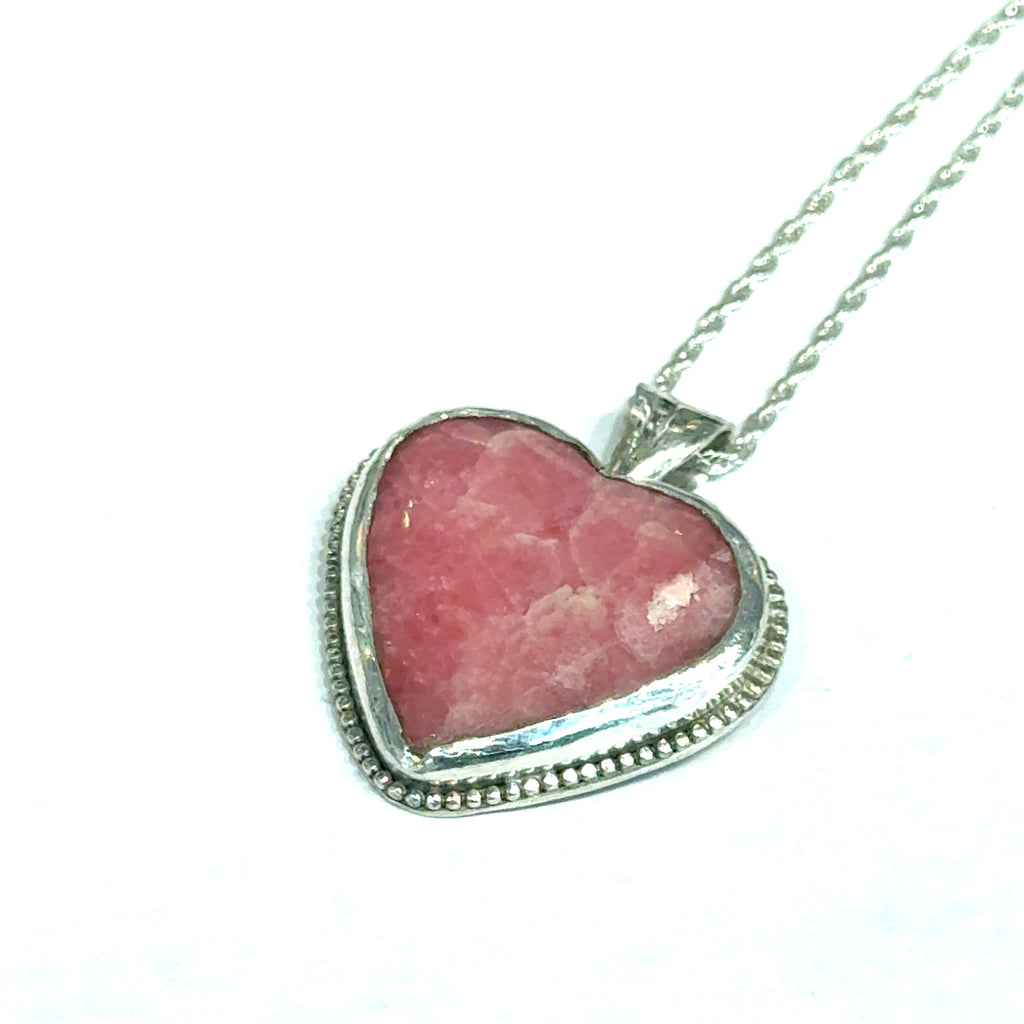 Pink Cobolto Calcite Heart-shaped gemstone pendant on a silver chain against a white background, front left angle hung overview. 