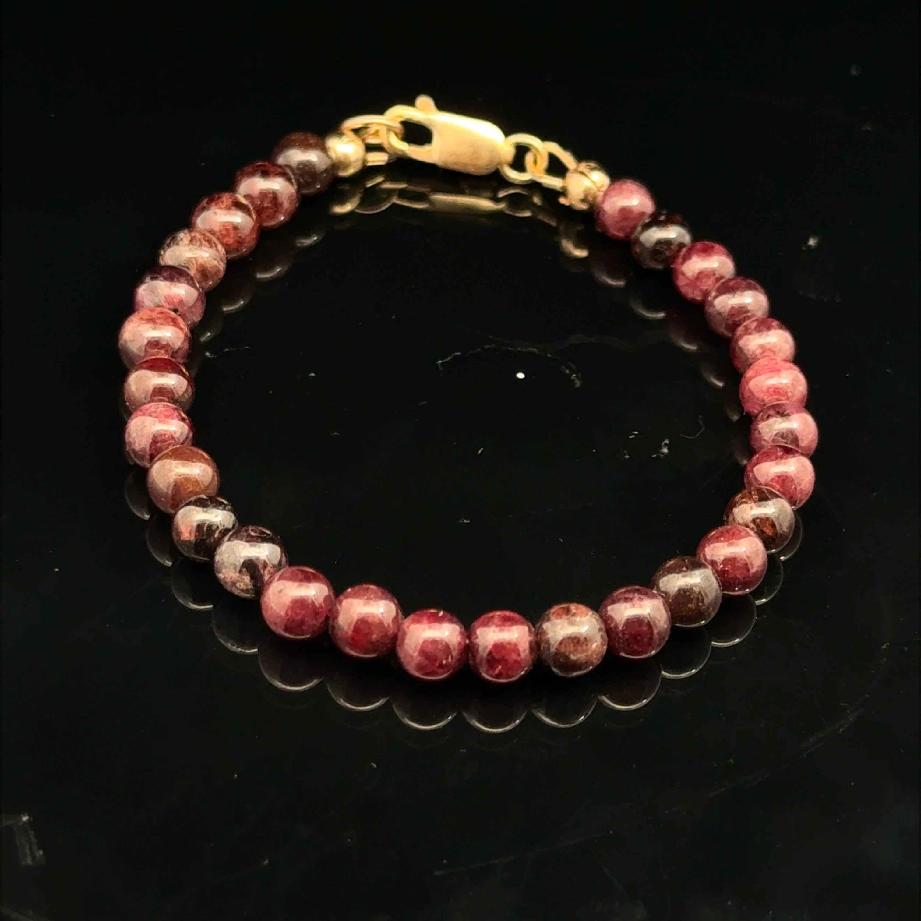 Red garnet gemstone beaded bracelet with a gold-filled lobster claw on a black background, front overview.