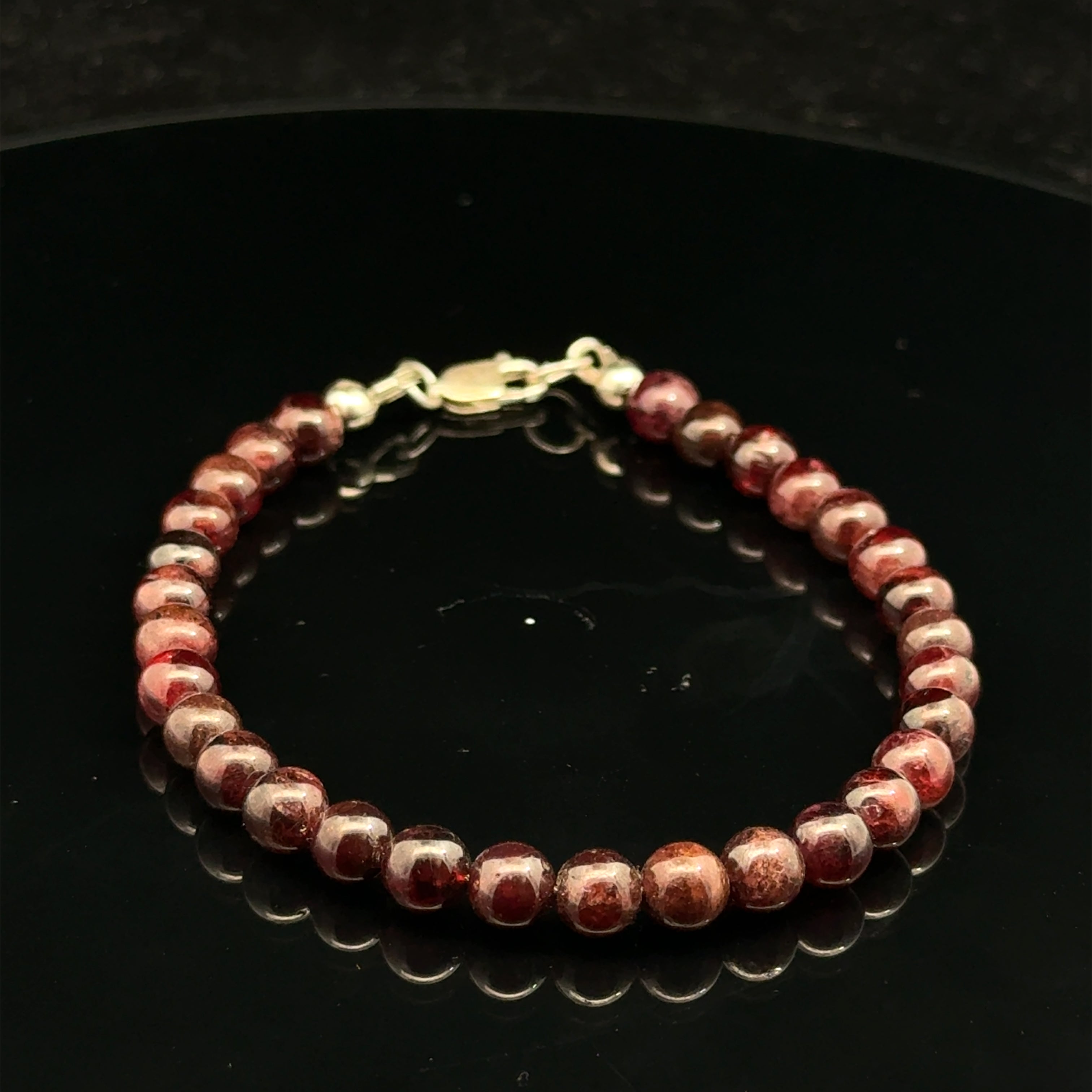 Red garnet gemstone beaded bracelet with a gold-filled lobster claw on a black background, front view.