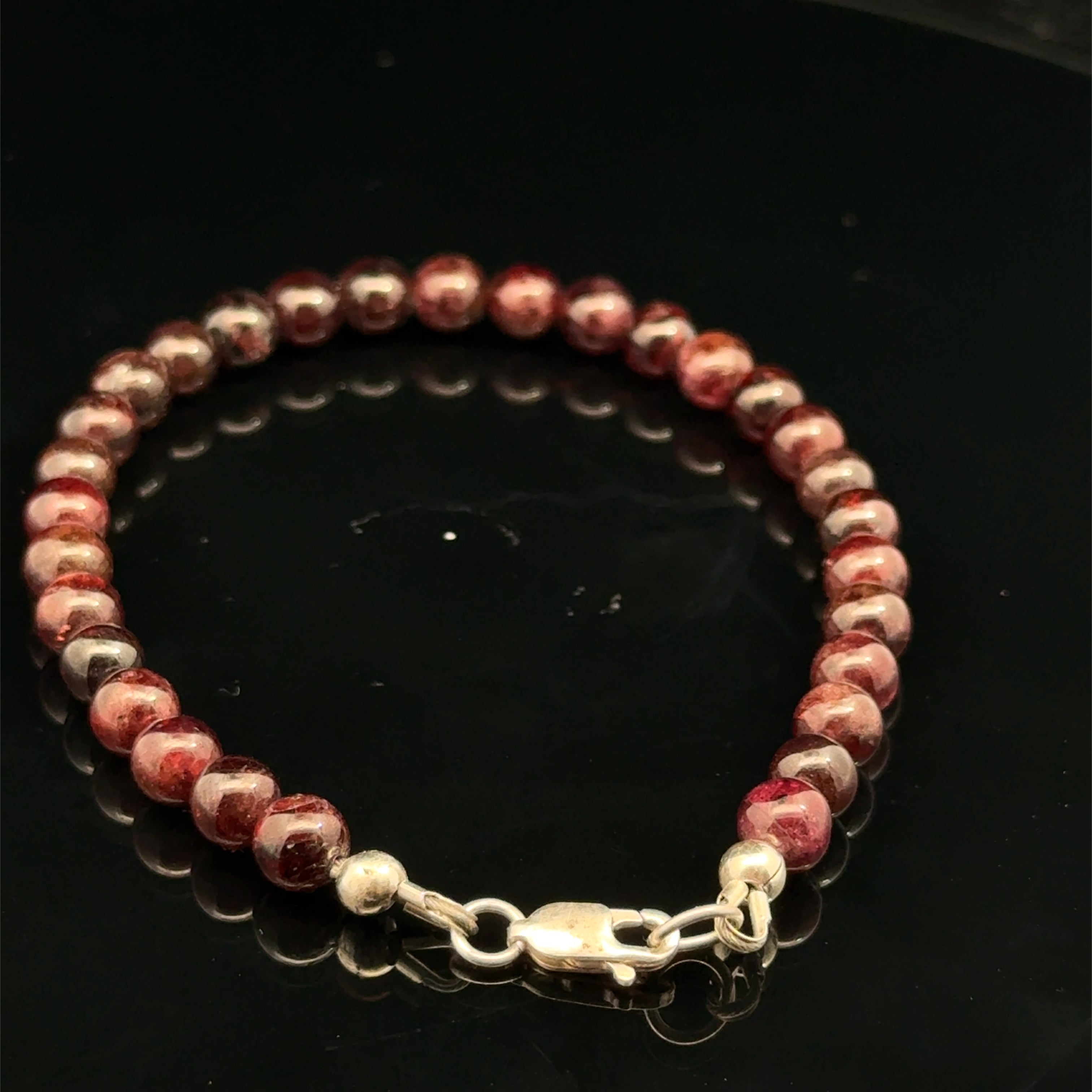 Red garnet gemstone beaded bracelet, with a sterling silver lobster claw on a black background, back view.
