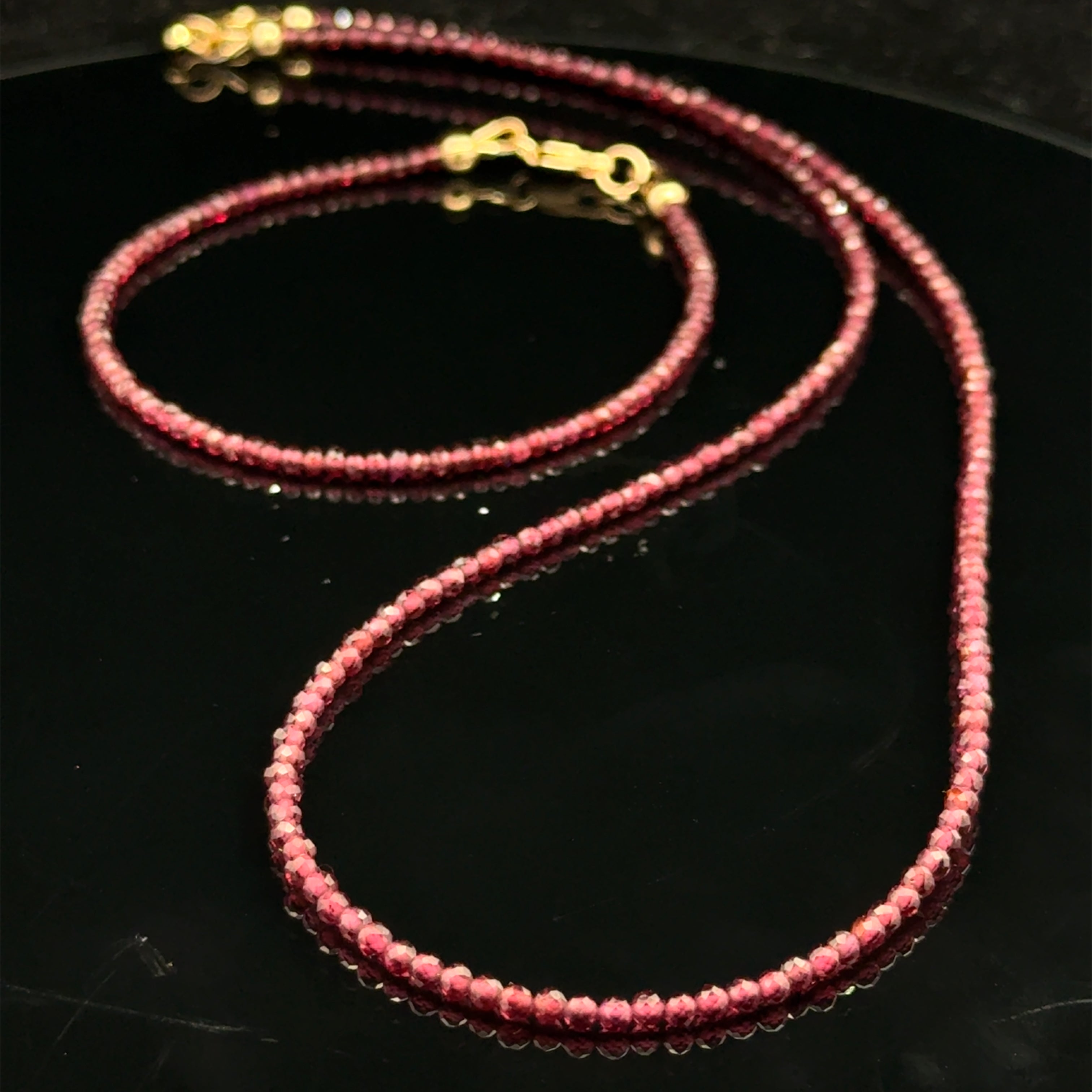 Red garnet gemstone beaded bracelet with its matching necklace and a gold-filled lobster claw on a black background, front overview.