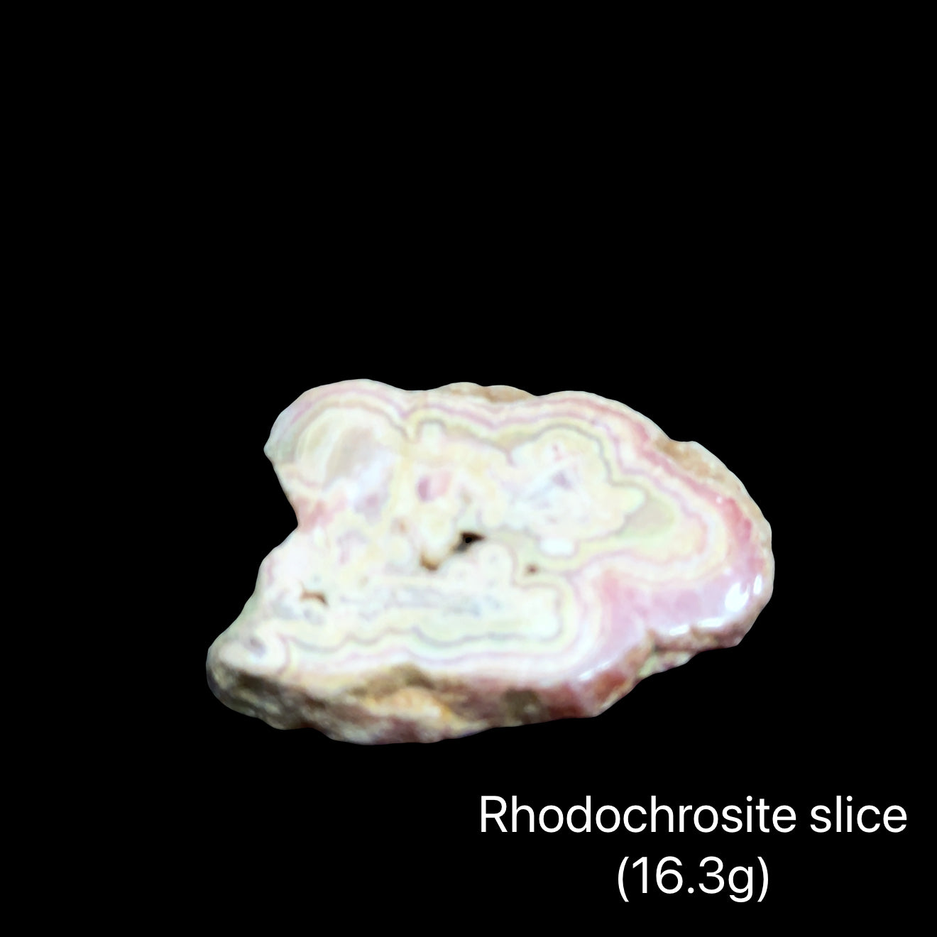 Rhodochrosite slice on a black background with weight indication (16.3g), front view.