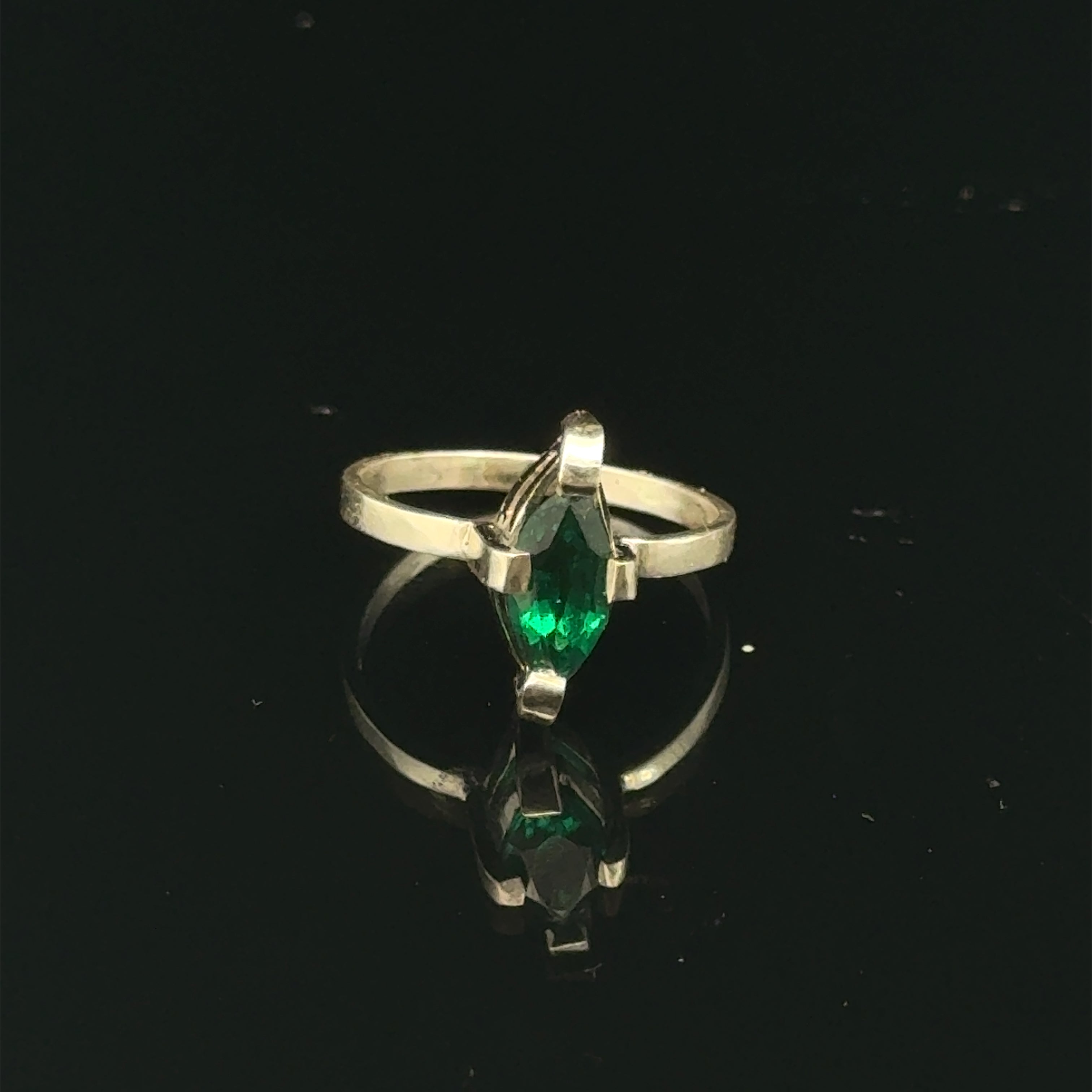 Sterling silver ring with faceted marquis emerald gemstone on a black background front, close up  view.