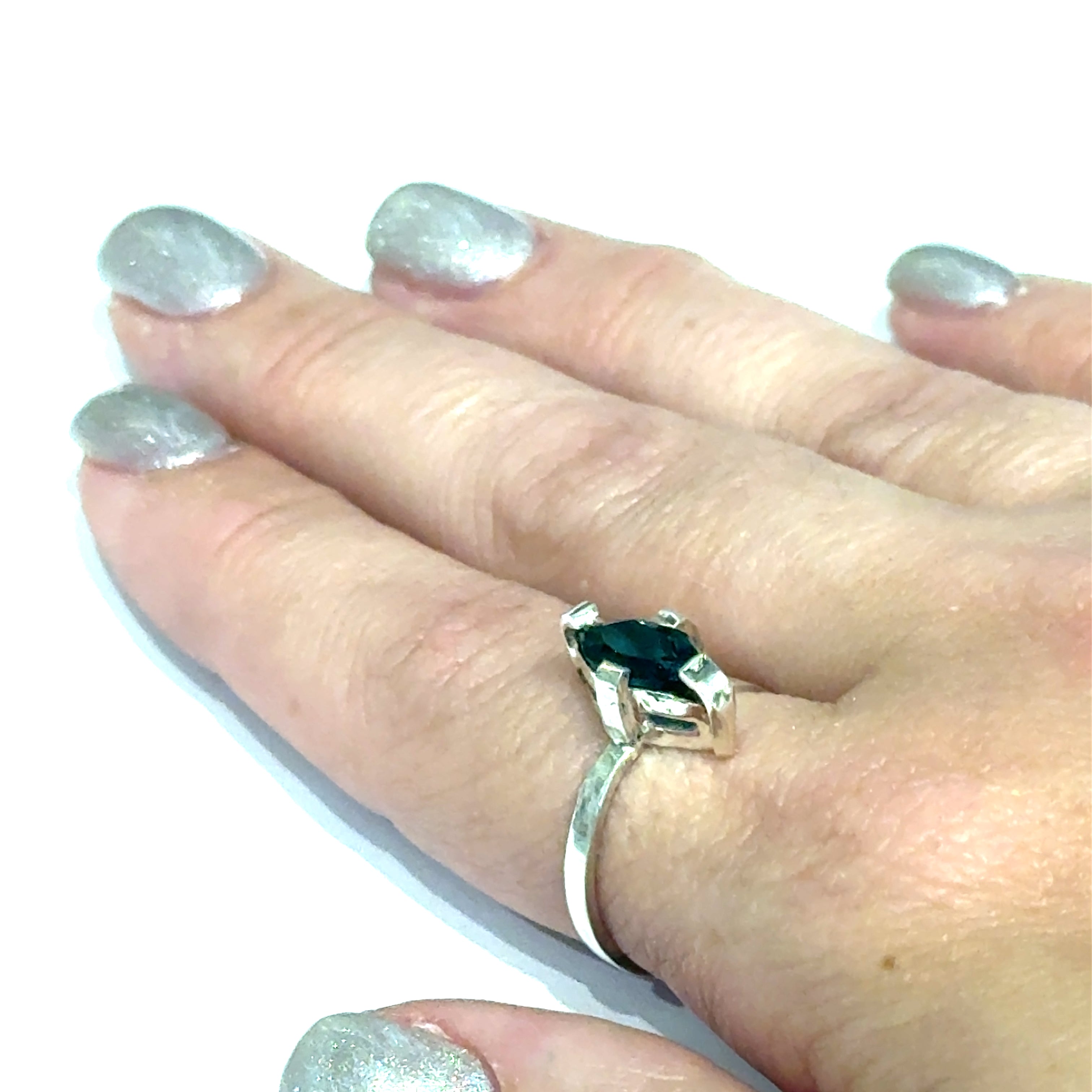 Sterling silver ring with faceted marquis emerald gemstone on a white background front, close up on a models finger view.
