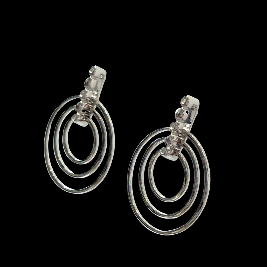 Sterling silver triple concentric circle stud earrings with three diamond accents on bar post on a black background, left angle view.