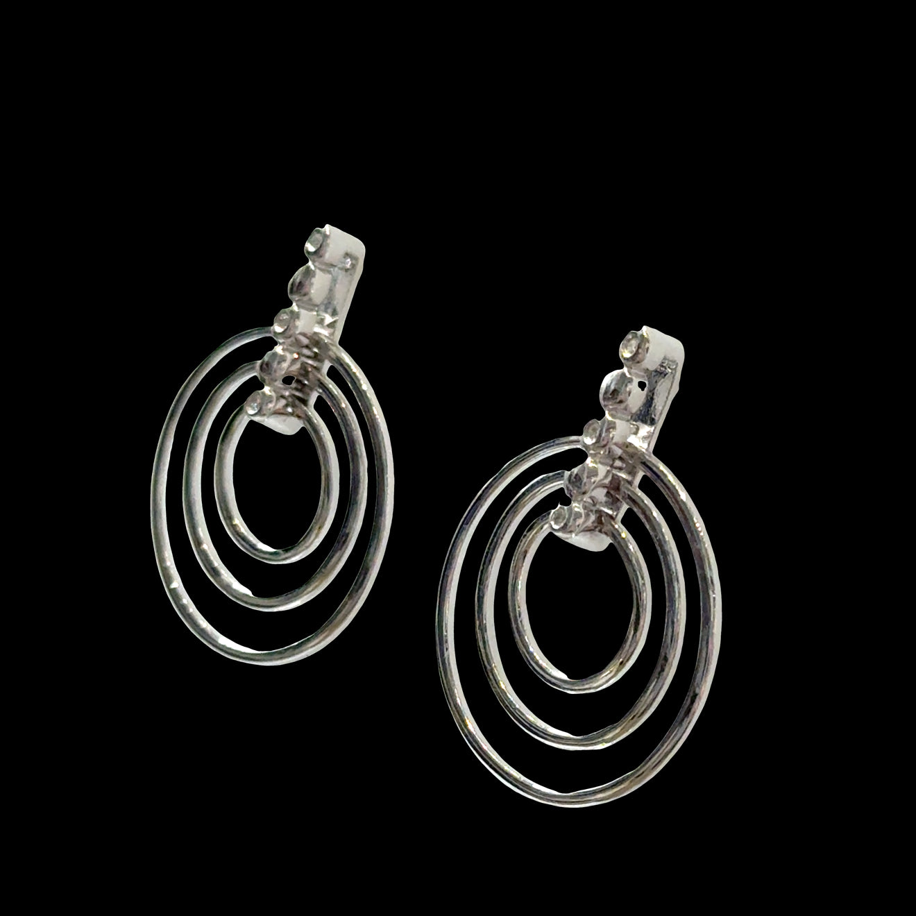 Sterling silver triple concentric circle stud earrings with three diamond accents on bar post on a black background, left angle view.