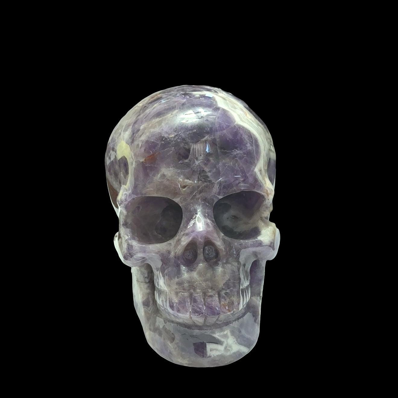 The largest of the two Trapiche Amethyst Gemstone carved skull on a black background,  front view. 